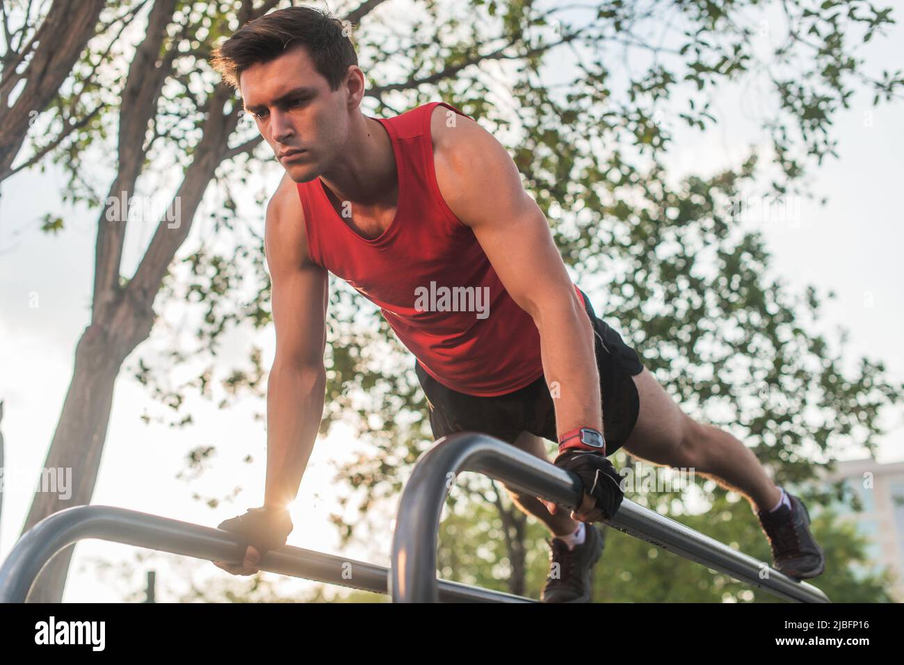 Fit young man doing push ups on horizontal bar outdoors. Stock Photo