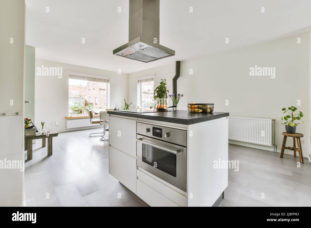 Built in oven in kitchen island under hood in spacious light apartment with white walls and laminate floor in daytime Stock Photo