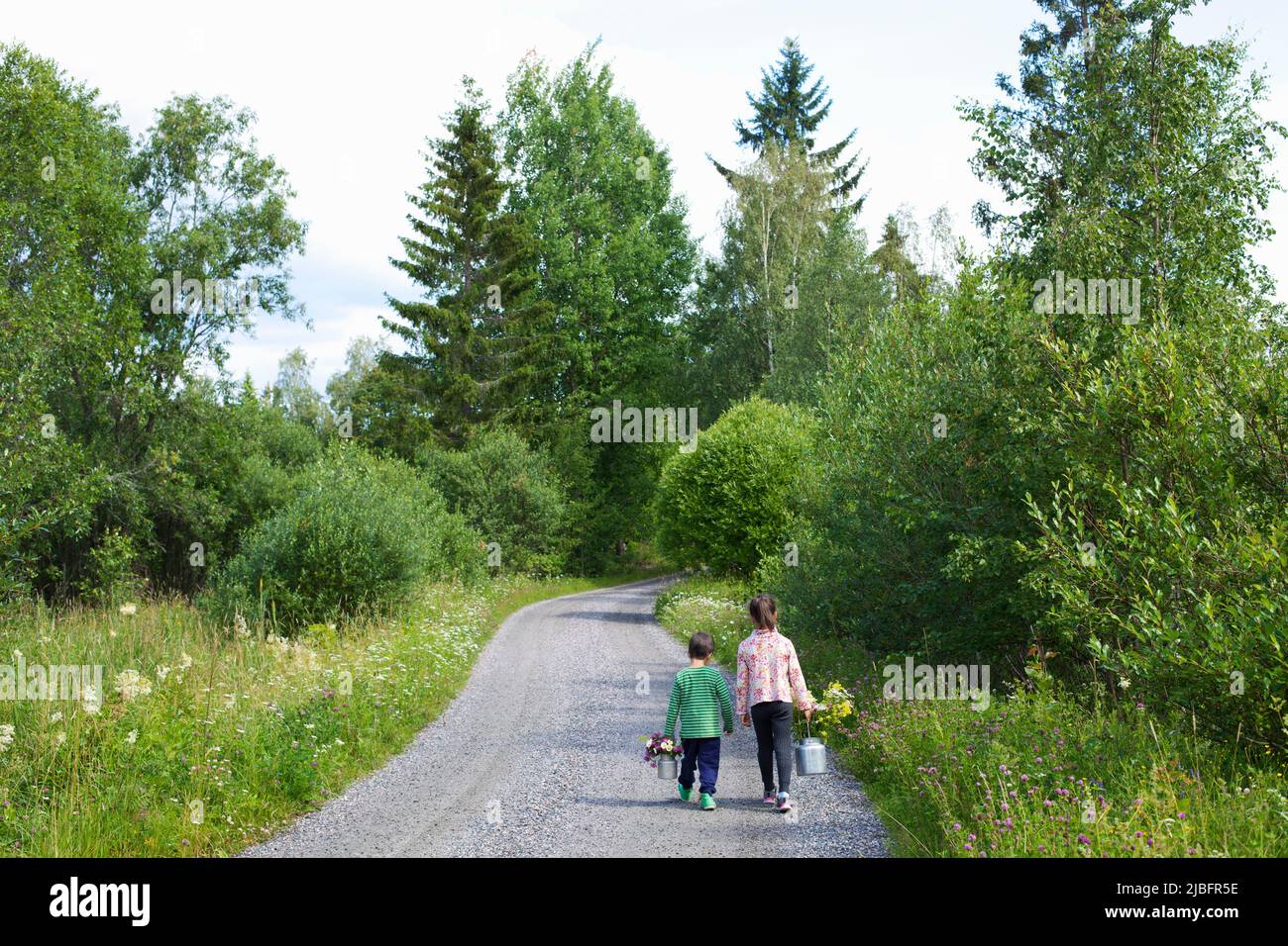 Siblings with flowers walking on road Stock Photo
