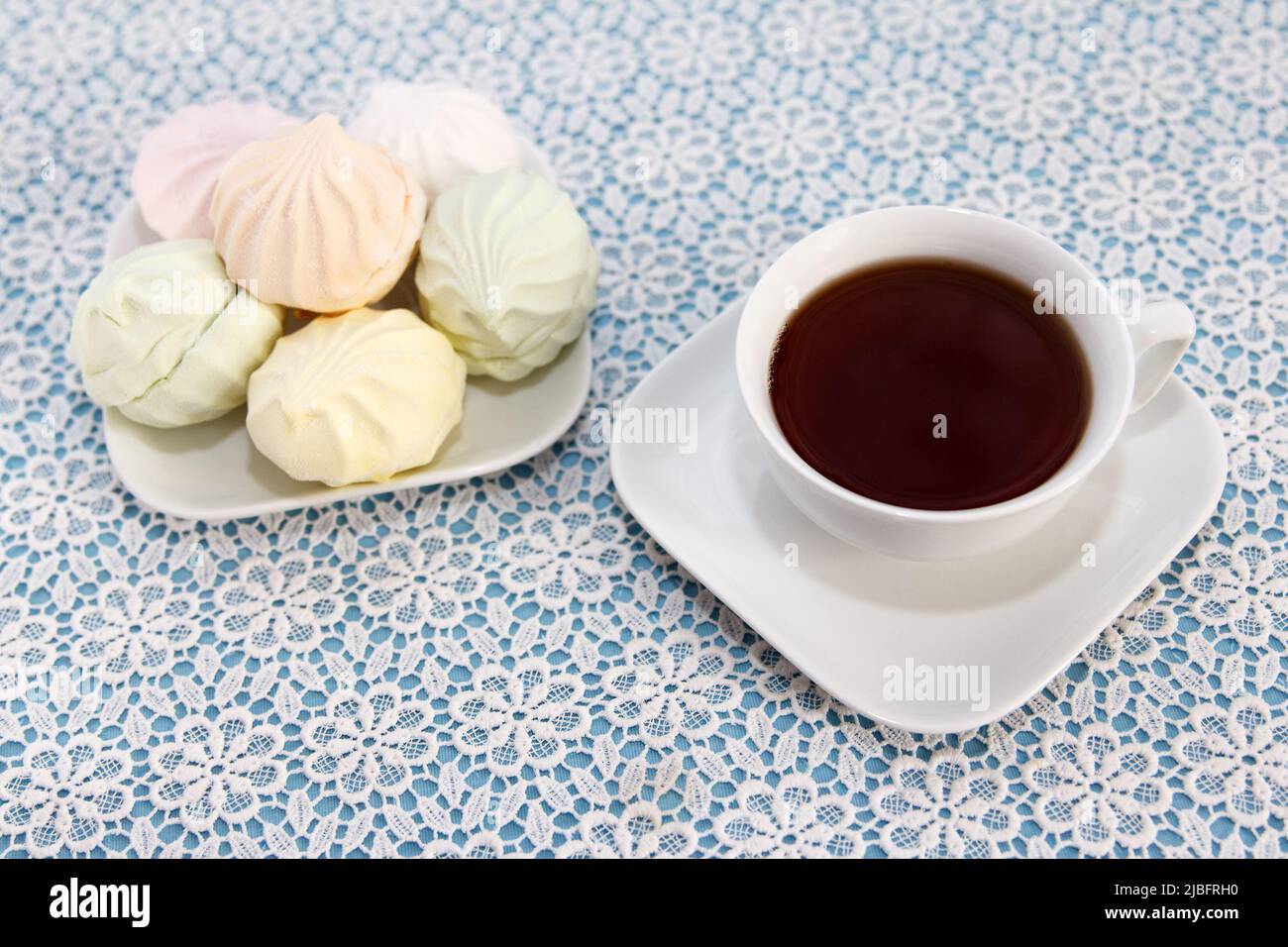 Traditional delicious brewed tea in a cup and air multicolored marshmallows lie on table, a sweet dessert Stock Photo
