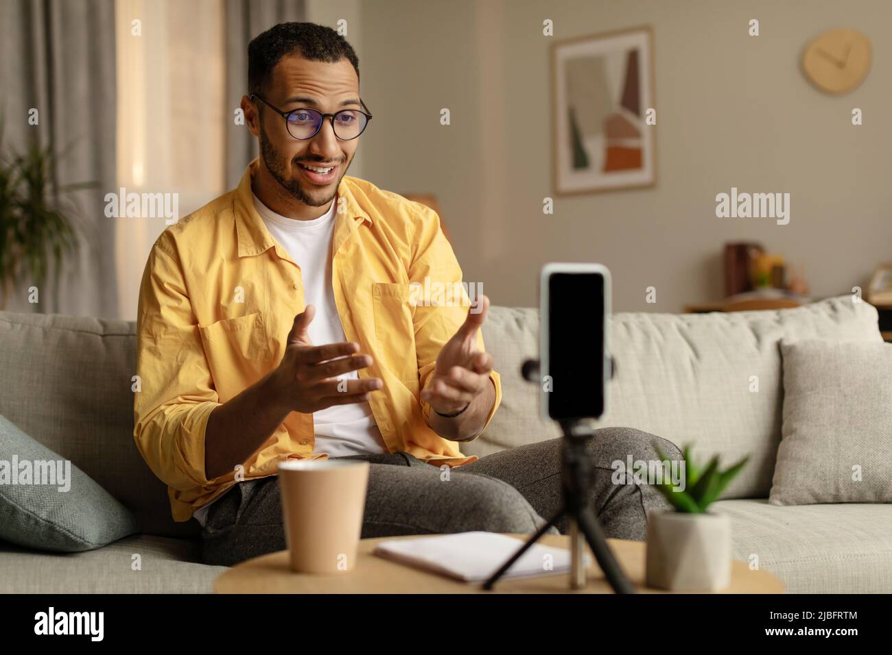 Positive millennial black teacher giving online lecture, using cellphone for communication with students from home Stock Photo