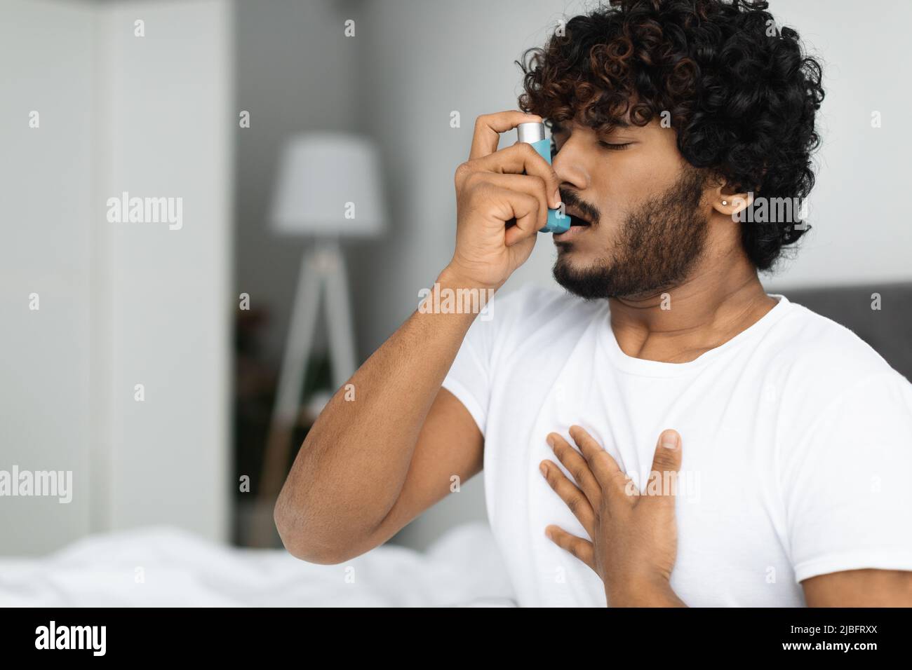 Indian guy suffering from asthma, using inhaler in bed Stock Photo