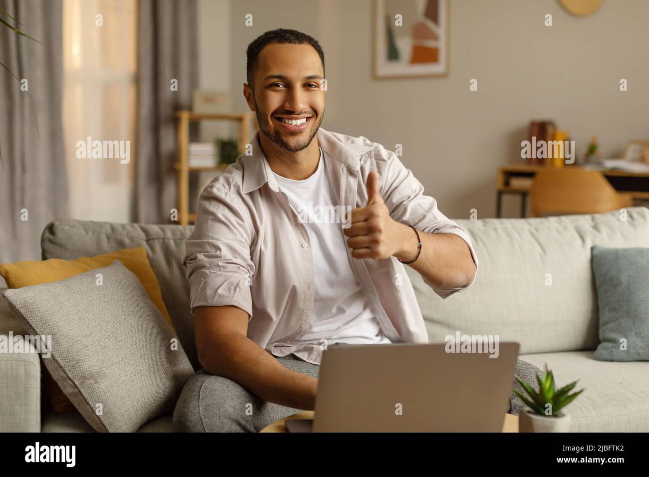 Happy young black guy working on laptop computer, showing thumb up ...