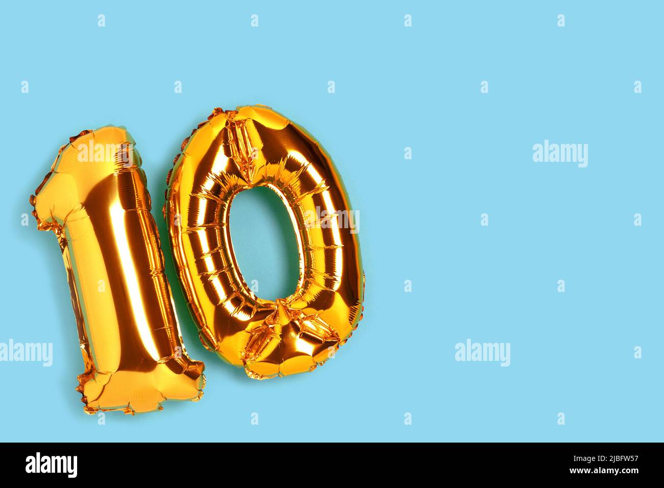 Number 10 golden balloon with copy space. Ten years anniversary celebration concept on a blue background. Stock Photo