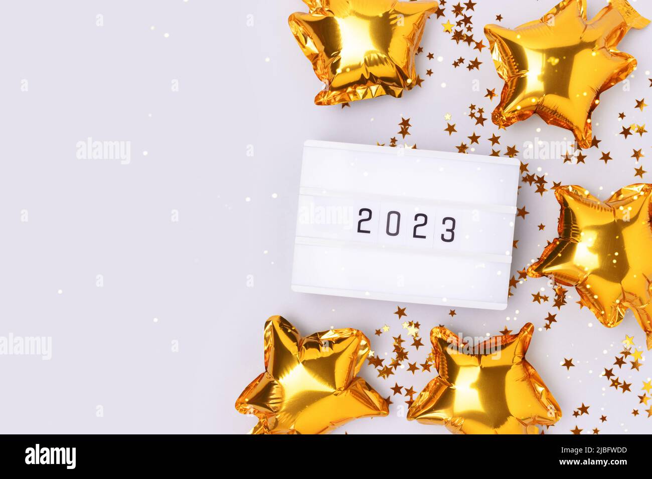 Lightbox with 2023 numbers on a blue background with copy space. Golden confetti and stars foil balloons. Stock Photo