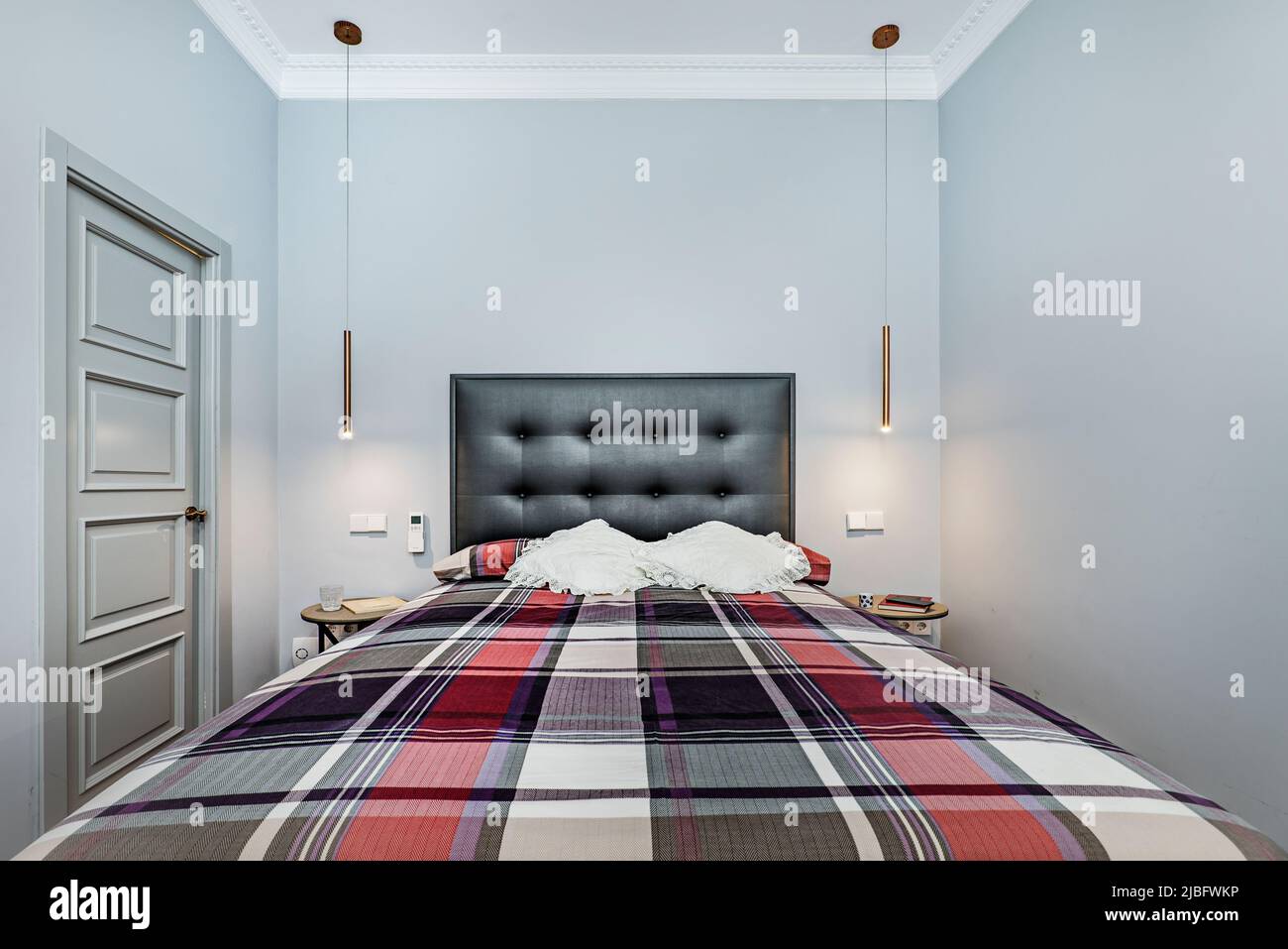 Nicely decorated double bedroom with bright fris fabric upholstered headboard, colorful square bedspread and gray wooden door to an en-suite bathroom Stock Photo