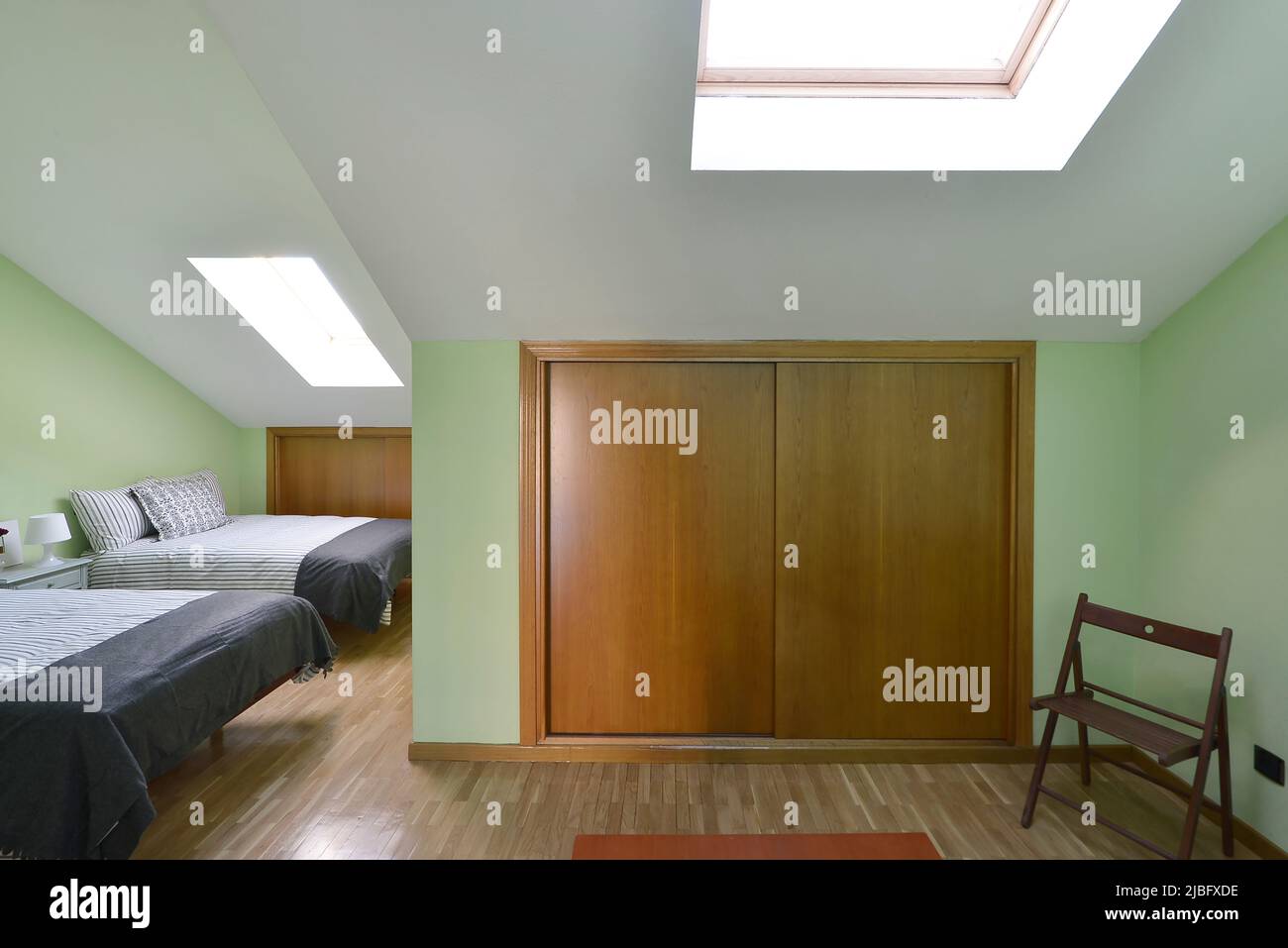 Bedroom in an attic room with two single beds with cushions, wooden