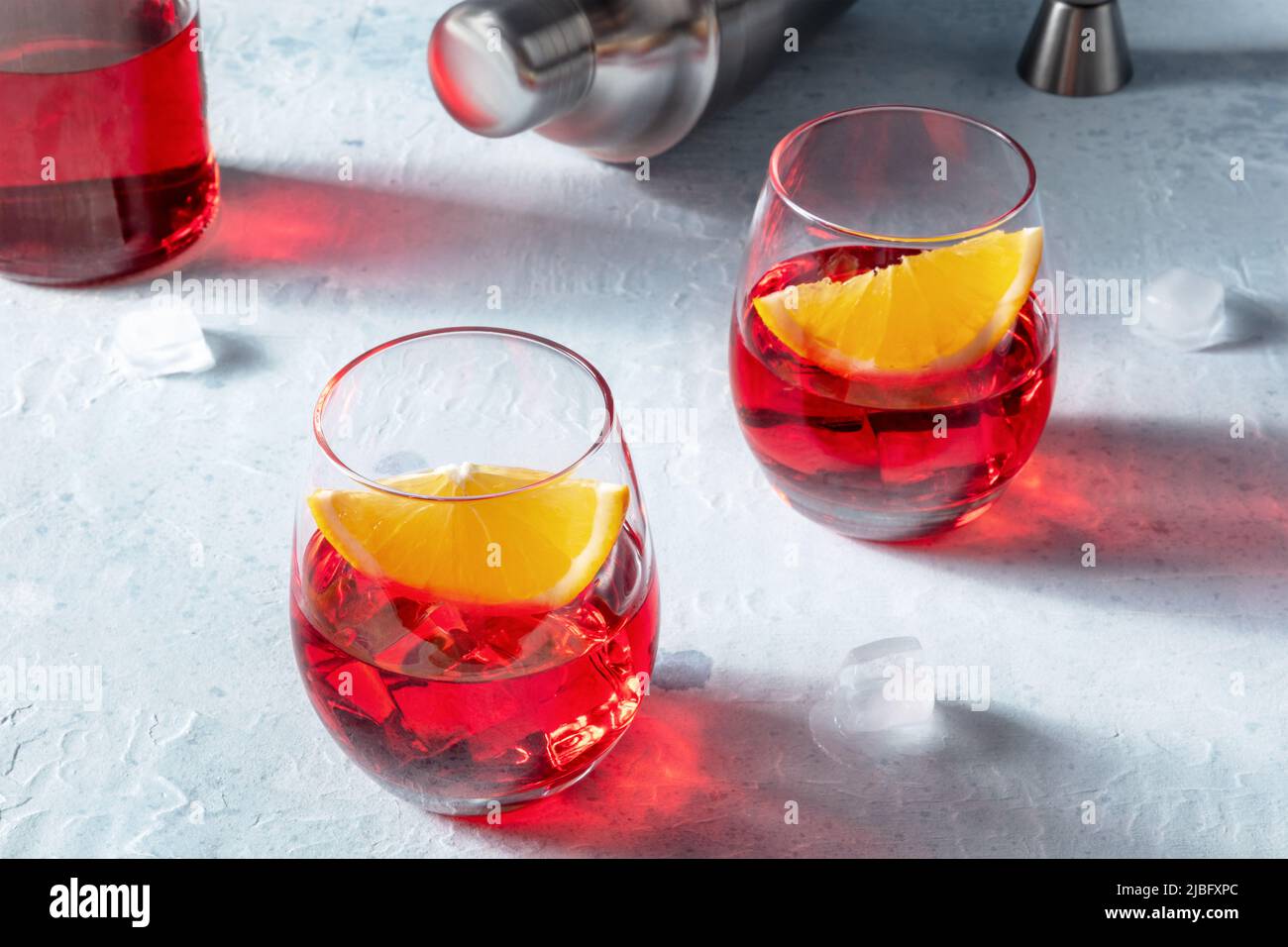Campari orange cocktails with a jigger and a shaker, with ice cubes and a bottle in the background, on a slate table Stock Photo