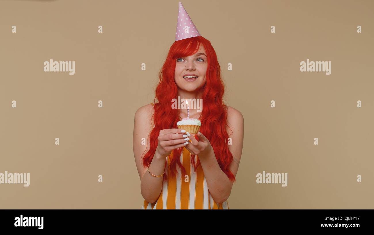 Happy redhead young woman in festive cone cap celebrating birthday