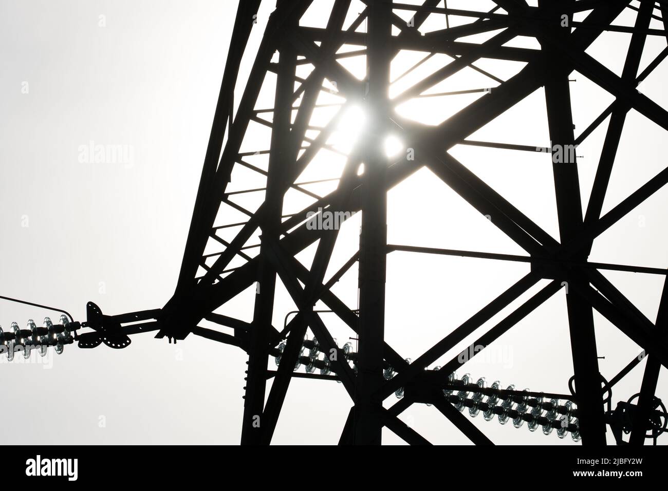 The sun shined behind the silhouette of the metal work of an electricity pylon in connection with the natural energy of the sun and man-made energy Stock Photo
