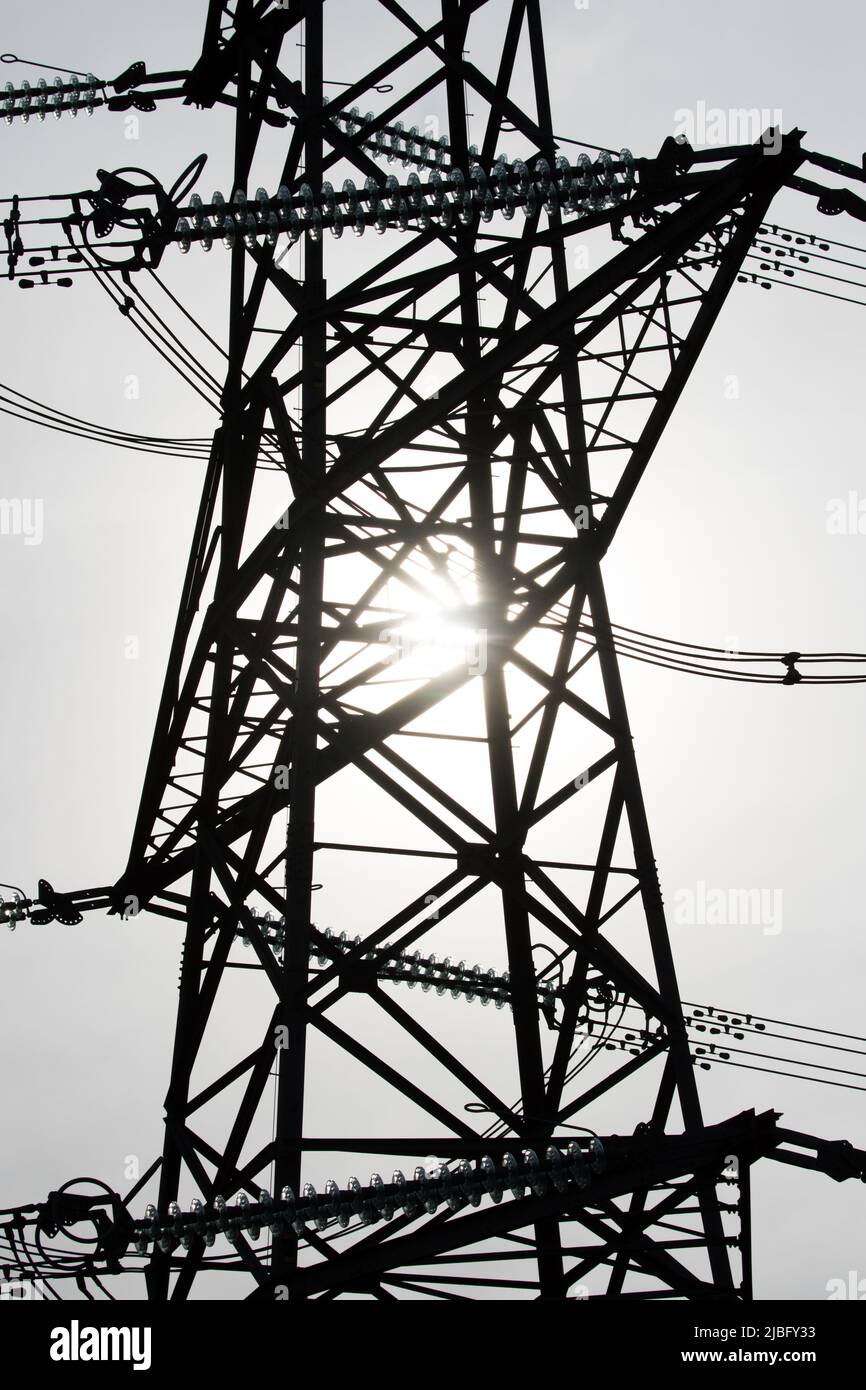 The sun shined behind the silhouette of the metal work of an electricity pylon in connection with the natural energy of the sun and man-made energy Stock Photo