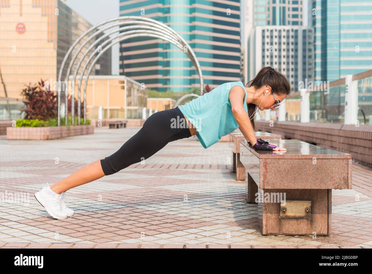 Fitness woman doing feet elevated pushups on a bench in the city