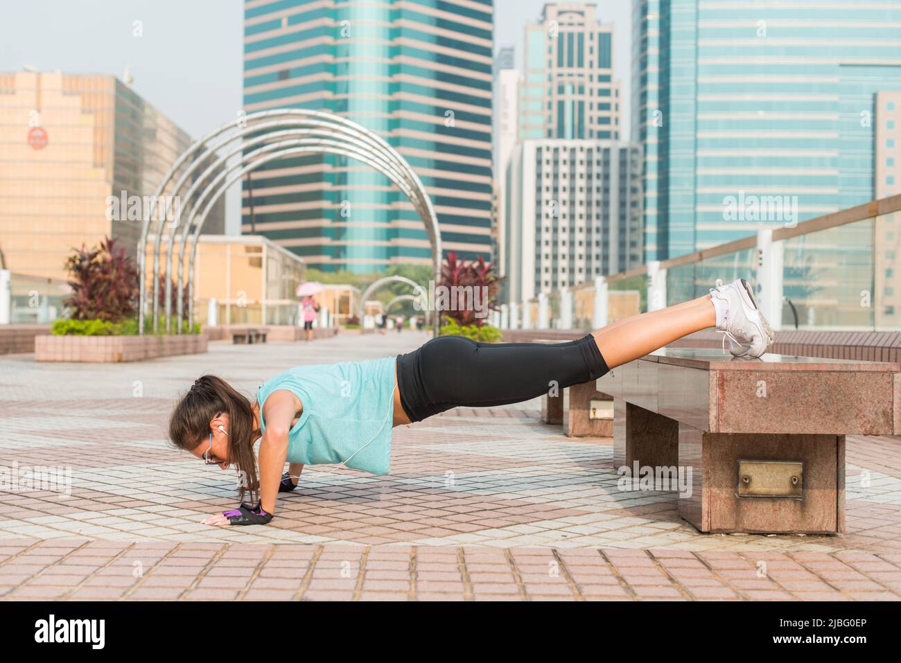 Fitness woman doing feet elevated pushups on a bench in the city. Sporty girl exercising