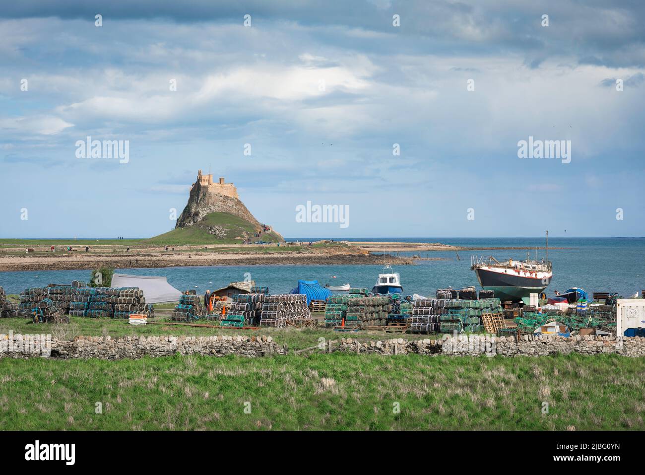 Holy Island Lindisfarne, view of fishing boats and lobster pots in Holy Island harbour with Lindisfarne Castle in the distance, Northumberland, UK Stock Photo