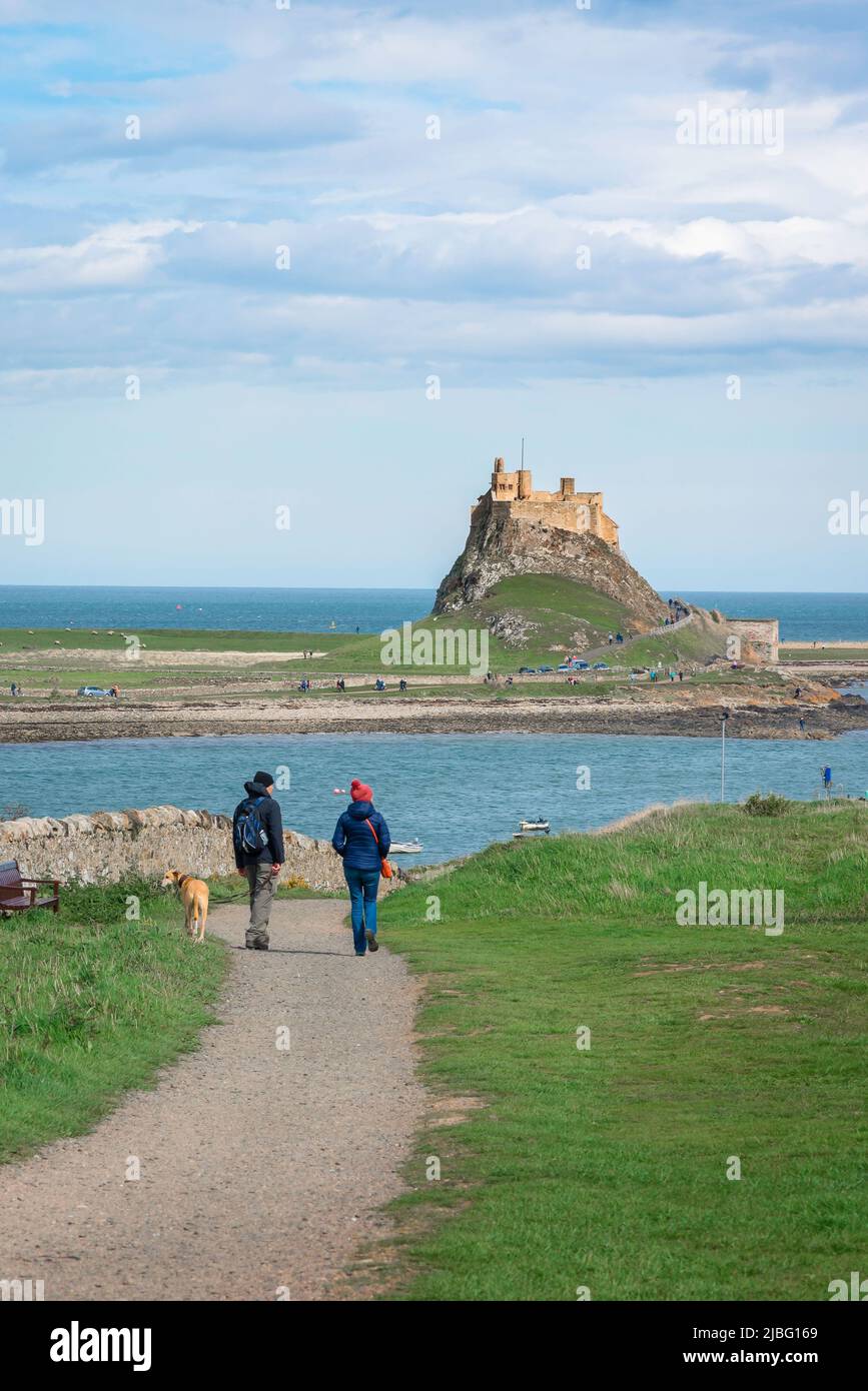 UK vacation, rear view in of a mature couple enjoying a leisurely walk with their dog while on holiday in Holy Island (Lindisfarne), Northumberland UK Stock Photo