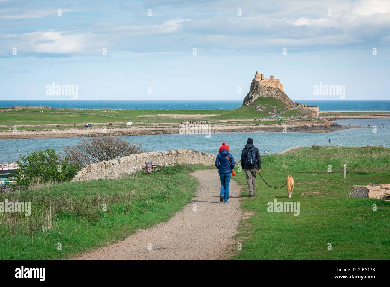 Northumberland holiday, view in summer of a mature couple enjoying a leisurely walk with their dog on Holy Island (Lindisfarne), Northumberland coast Stock Photo