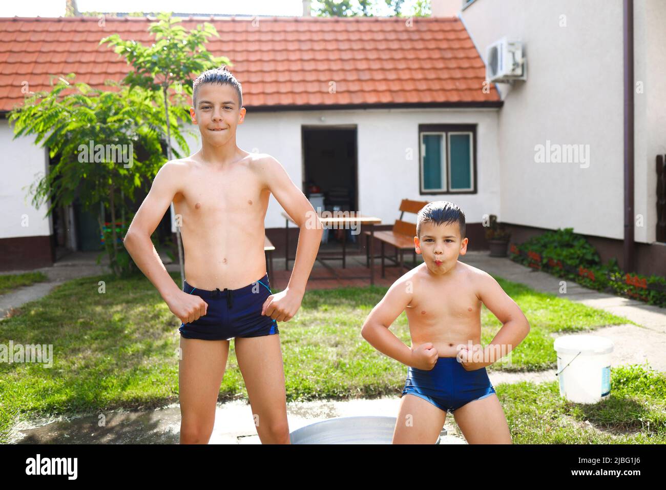Two brothers goofing around and flexing muscles while playing with water during their summer break Stock Photo
