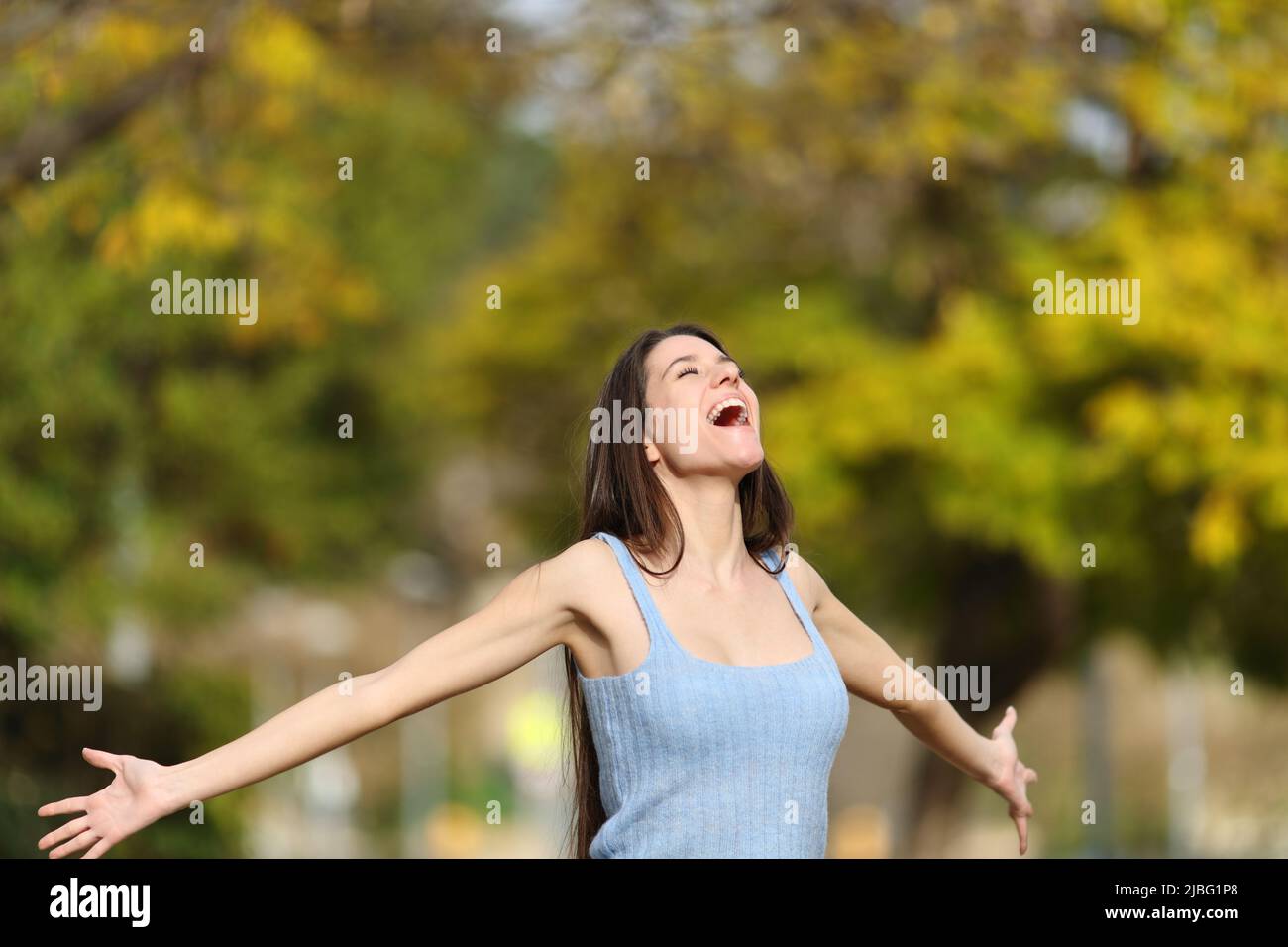 Excited teen screaming to the air outstretching arms standing in a park Stock Photo