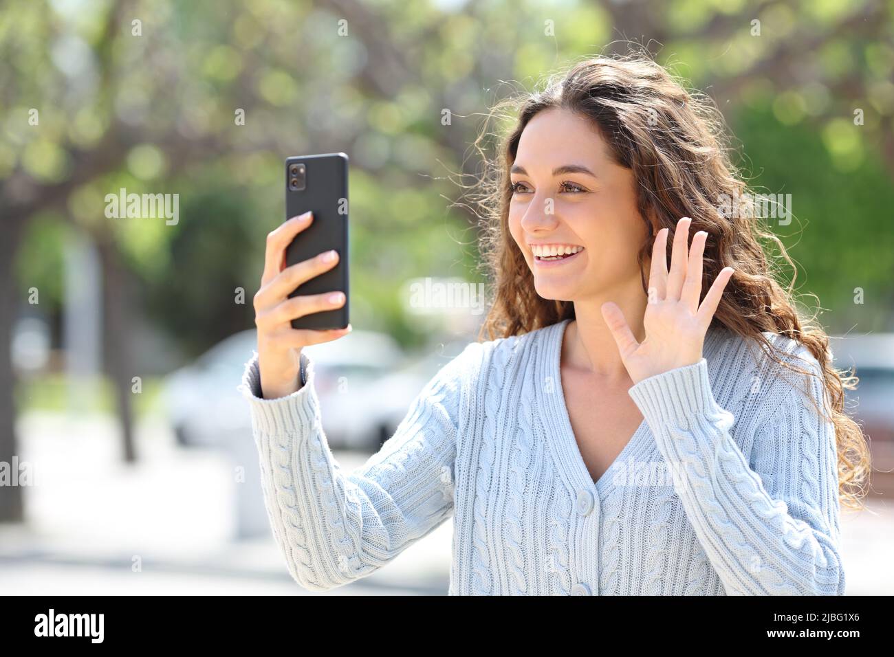 Happy woman greeting at cell phone in a video call in the street Stock Photo