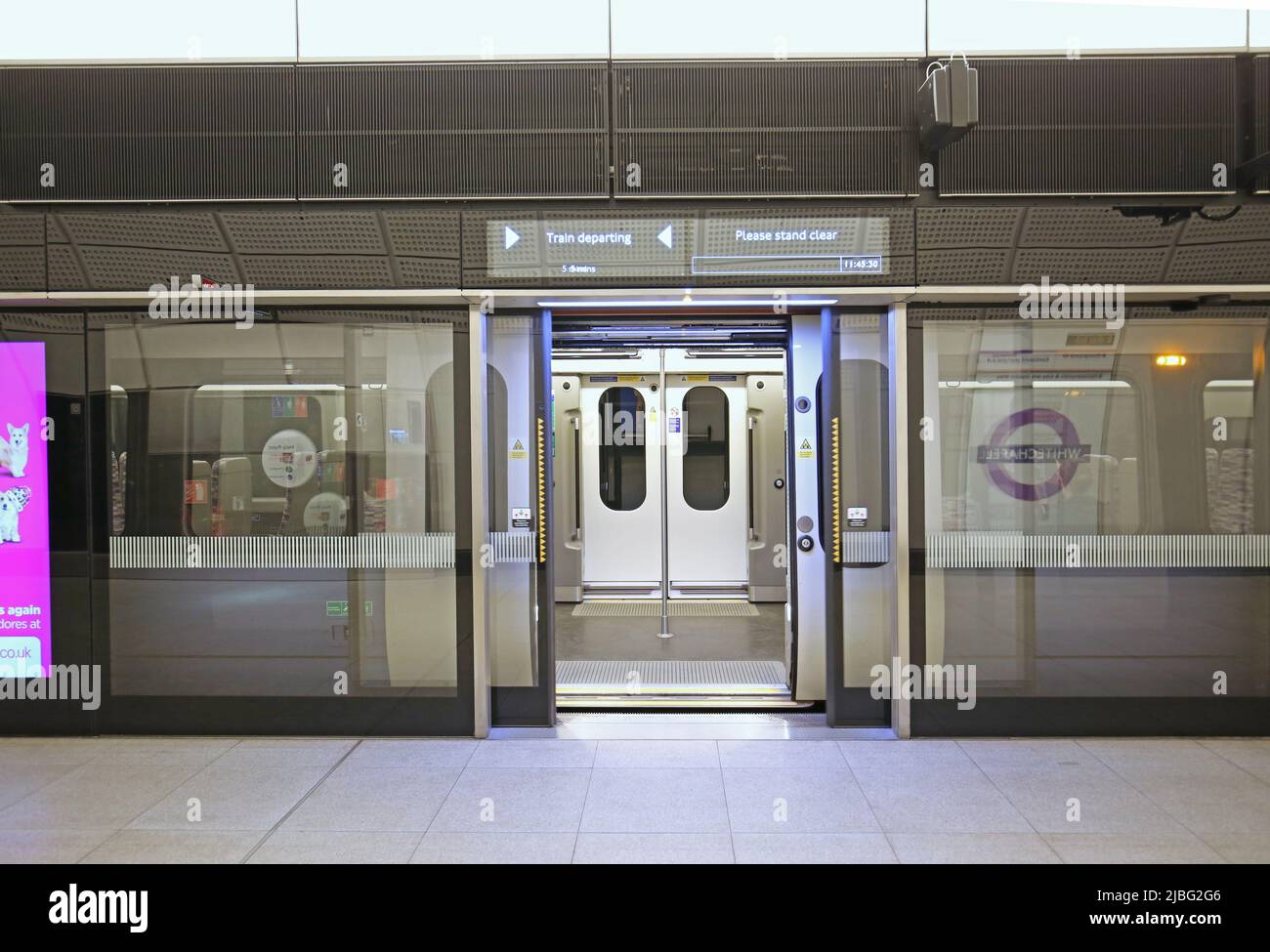 London, UK. A train on the new Elizabeth Line (Crossrail) waits at Whitechapel Station. Train and safety screen doors open, information sign above. Stock Photo