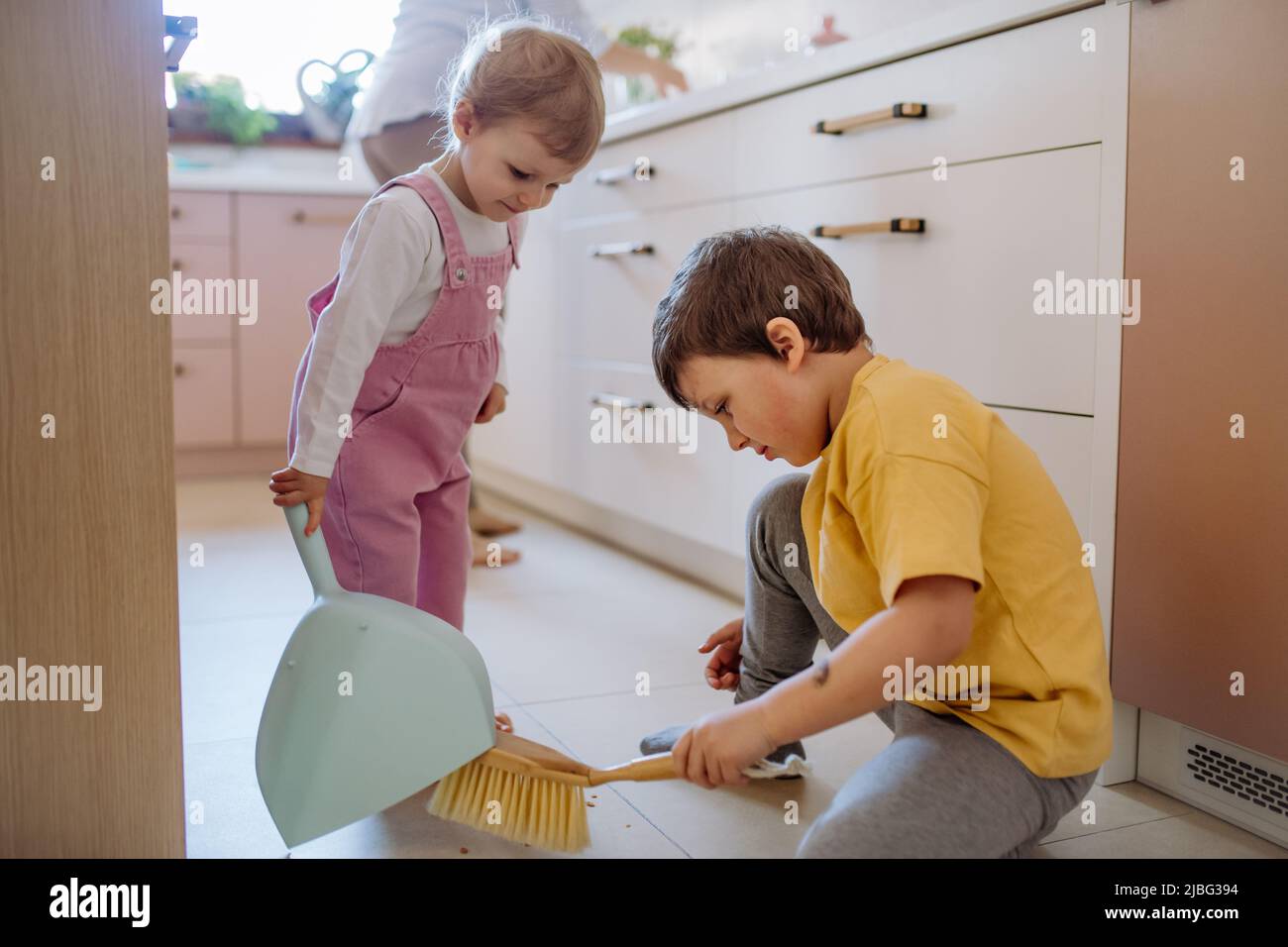 Little boy and girl helping to clean house using pan and brush as they