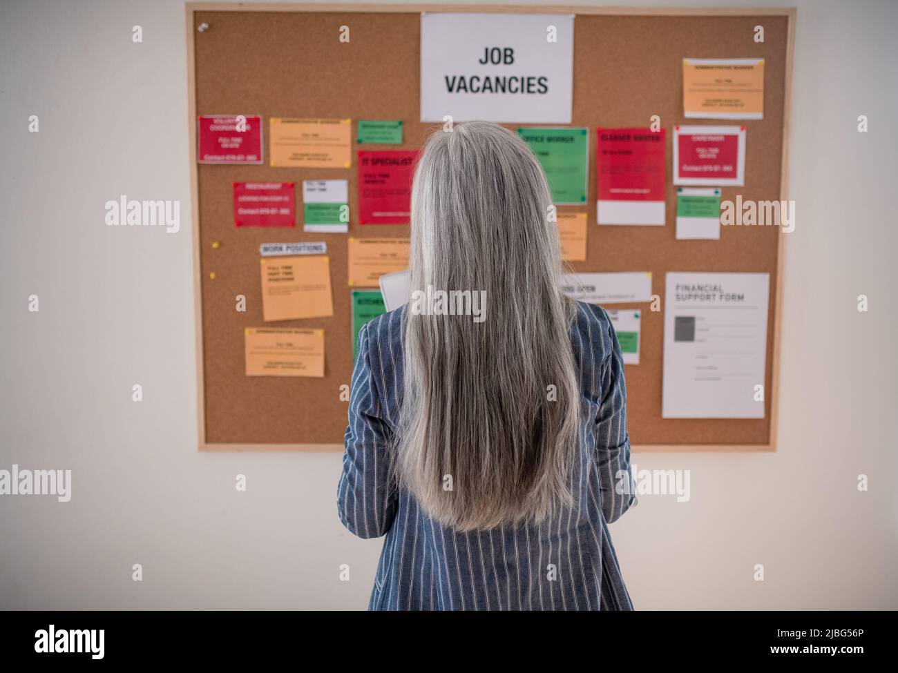 Job center employee standing in front of employment noticeboard. Rear