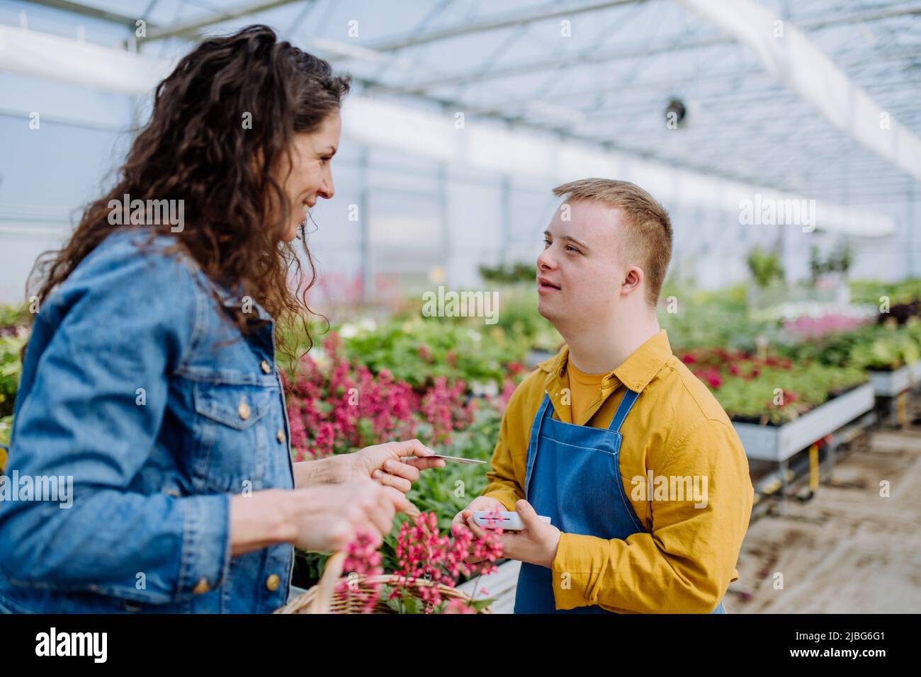 Happy young employee with Down syndrome working in garden centre, taking payment from customer. Stock Photo