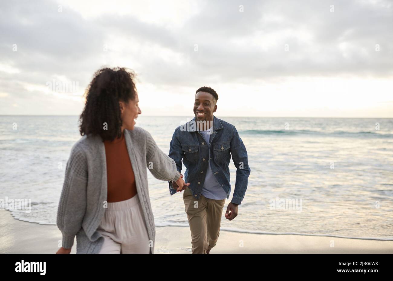 Smiling young multiethnic couple running hand in hand on a sandy beach Stock Photo