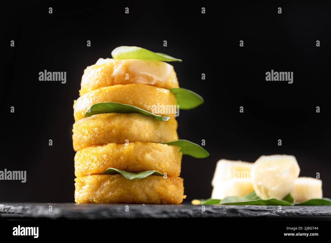 Italian porridge fried in the form of polenta pancakes on a black background with macarella cheese and spinach Stock Photo