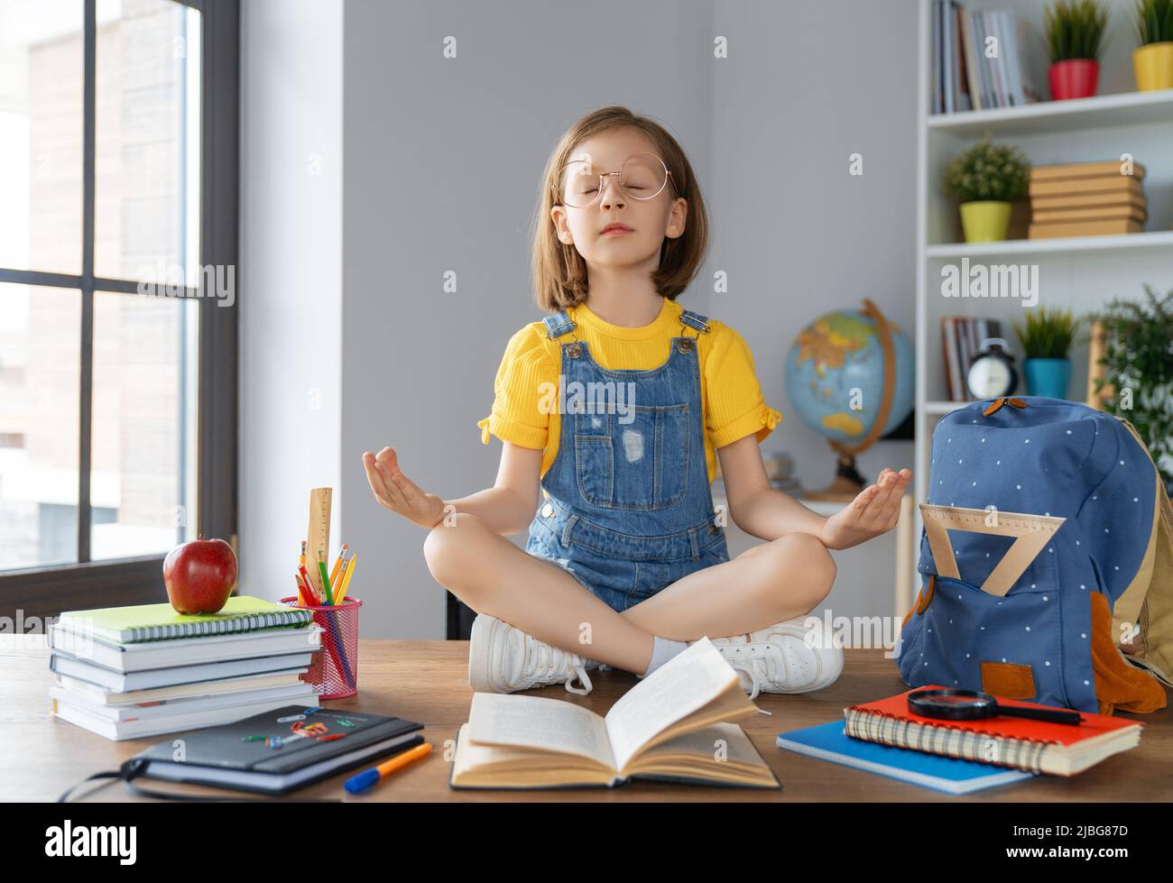 Back to school! Cute industrious child is meditating sitting at a desk indoors. Kid is learning in class or lesson. Stock Photo