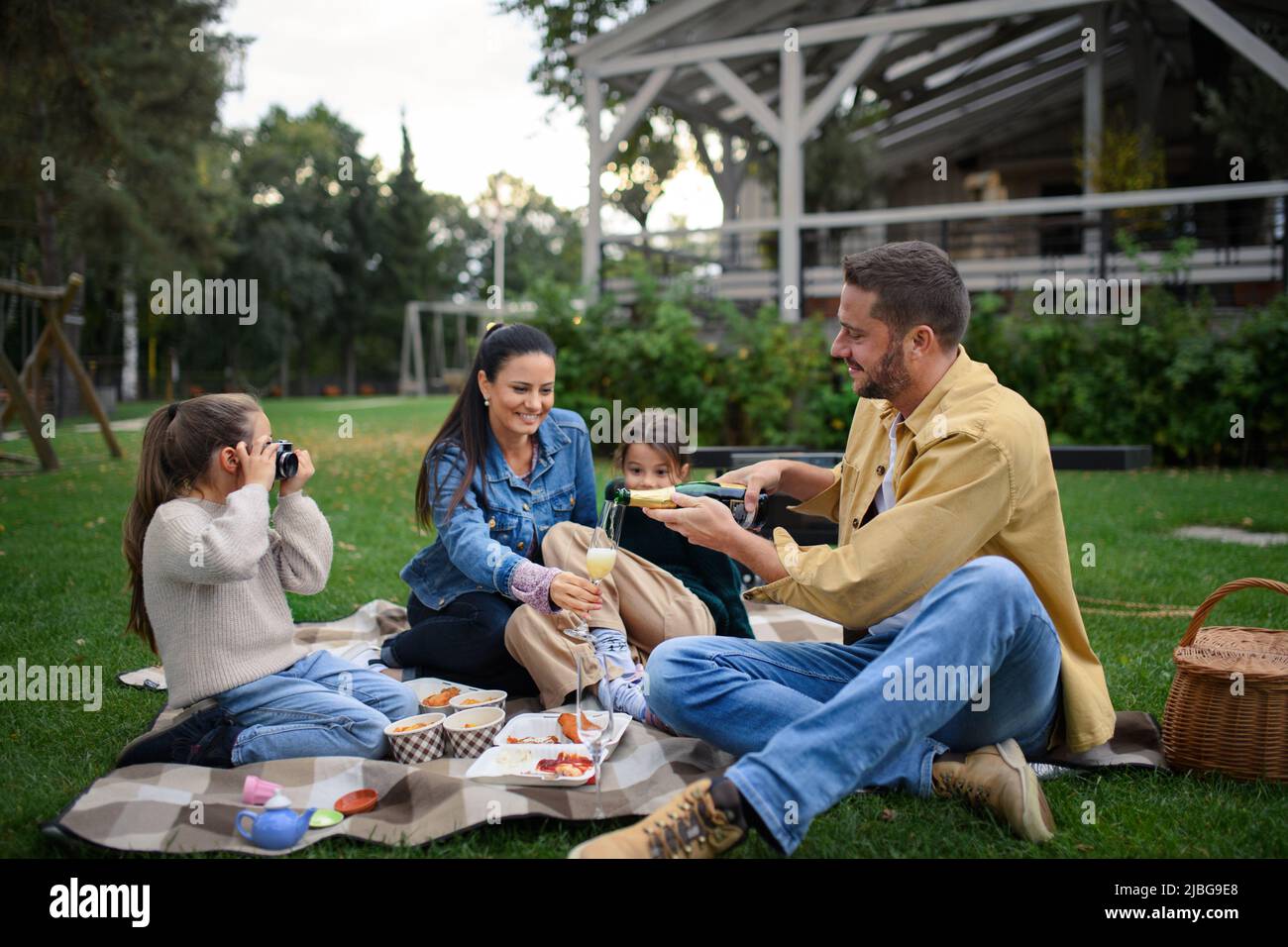 Happy young family sitting on blanket and having take away picnic outdoors in restaurant area. Stock Photo