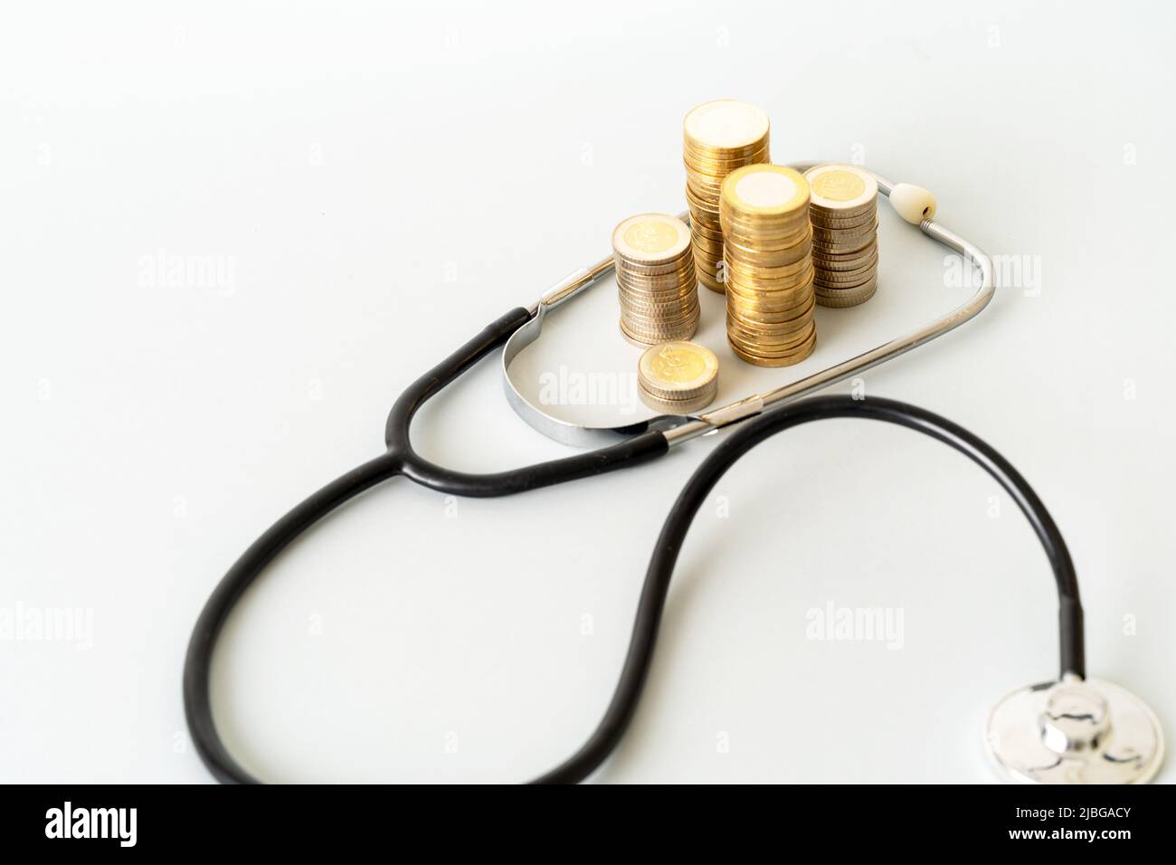 Close up photo of stethoscope and stacked coins on isolated background. Concept of rising costs of healthcare expenses. Stock Photo