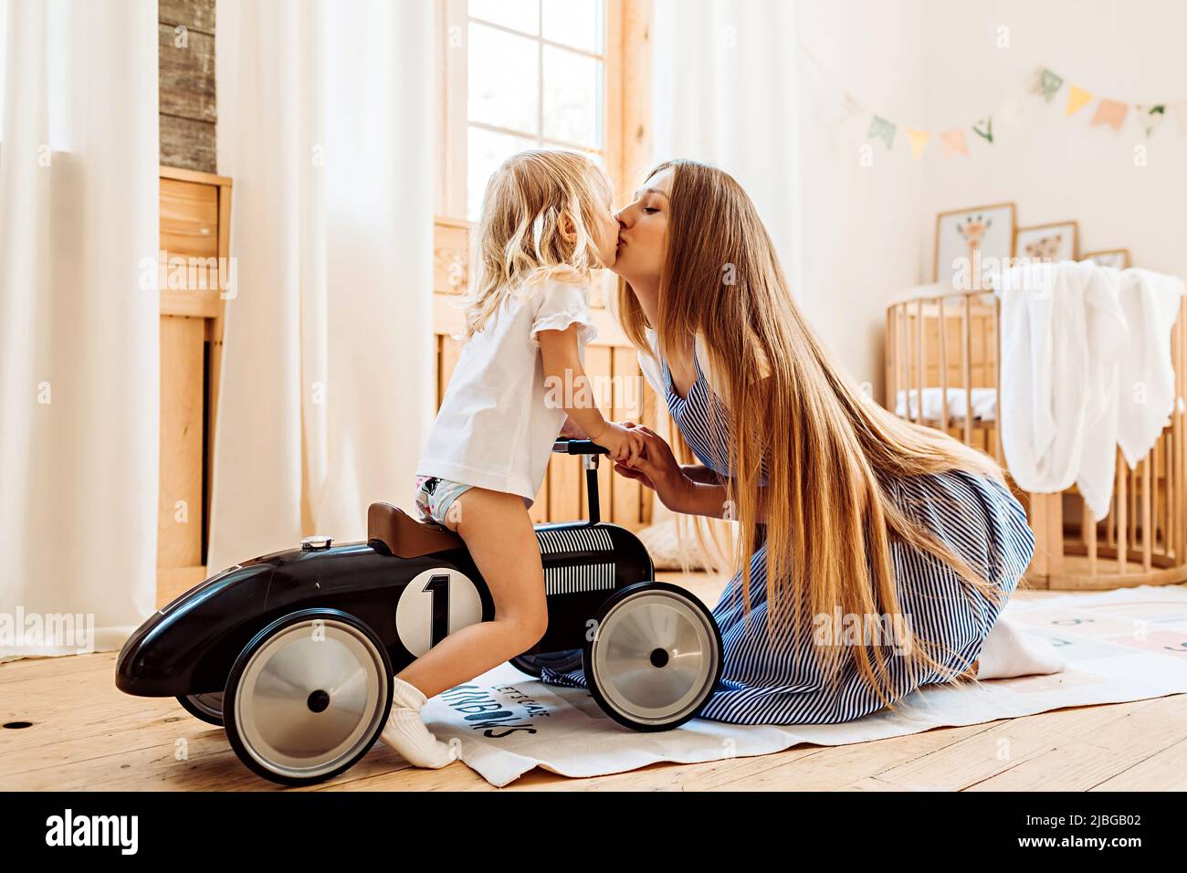 A young mother kisses her little daughter while playing at home. Family leisure lifestyle image Stock Photo