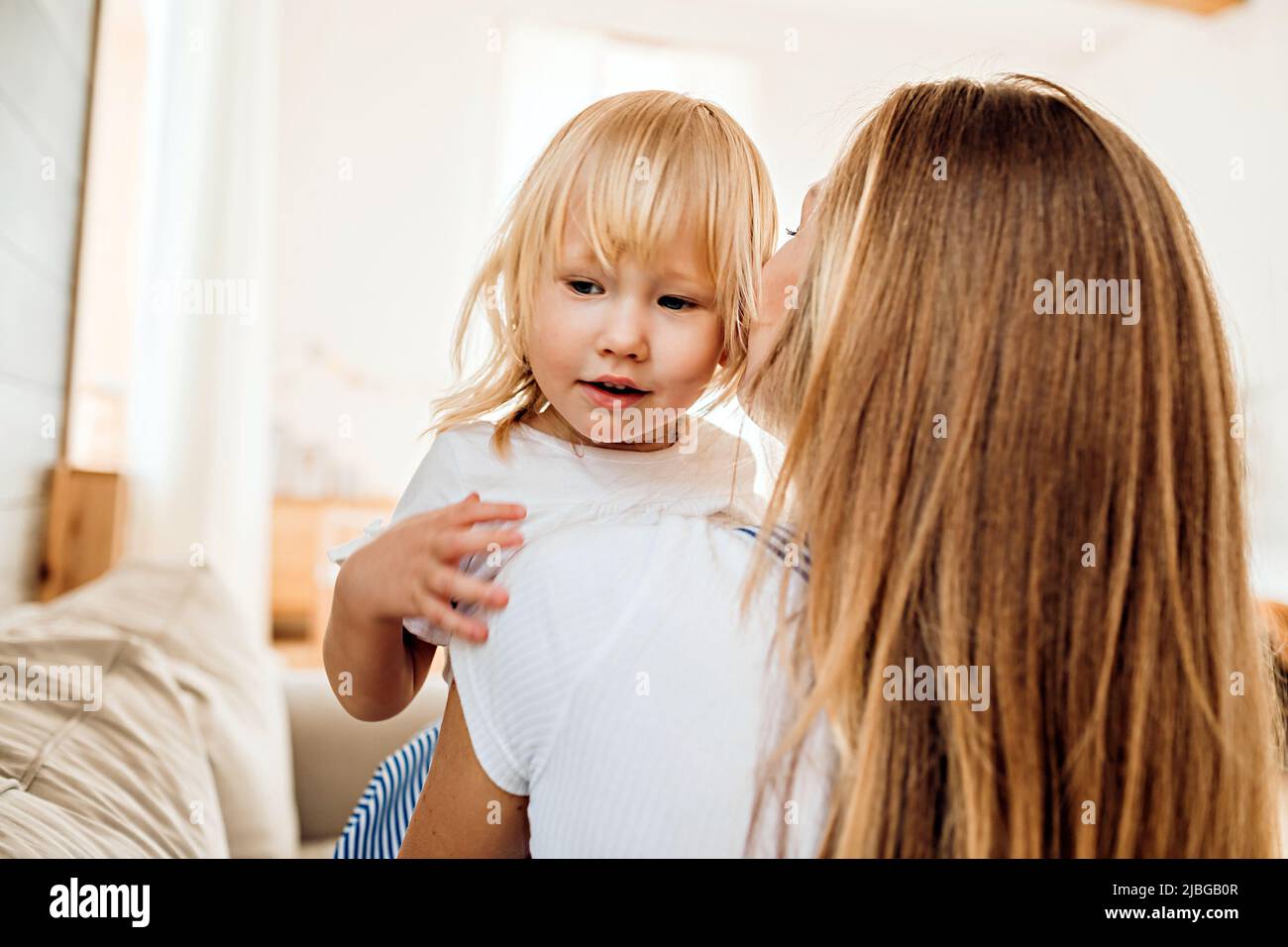 A young mother kisses her little daughter while playing at home. Family leisure lifestyle image Stock Photo