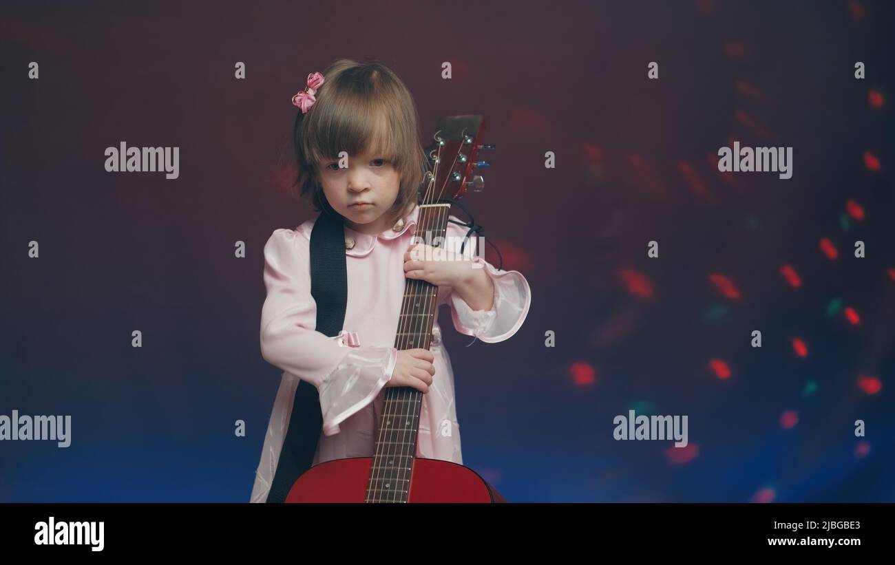 Little girl in a pink vintage dress plays an acoustic guitar like a double bass Stock Photo