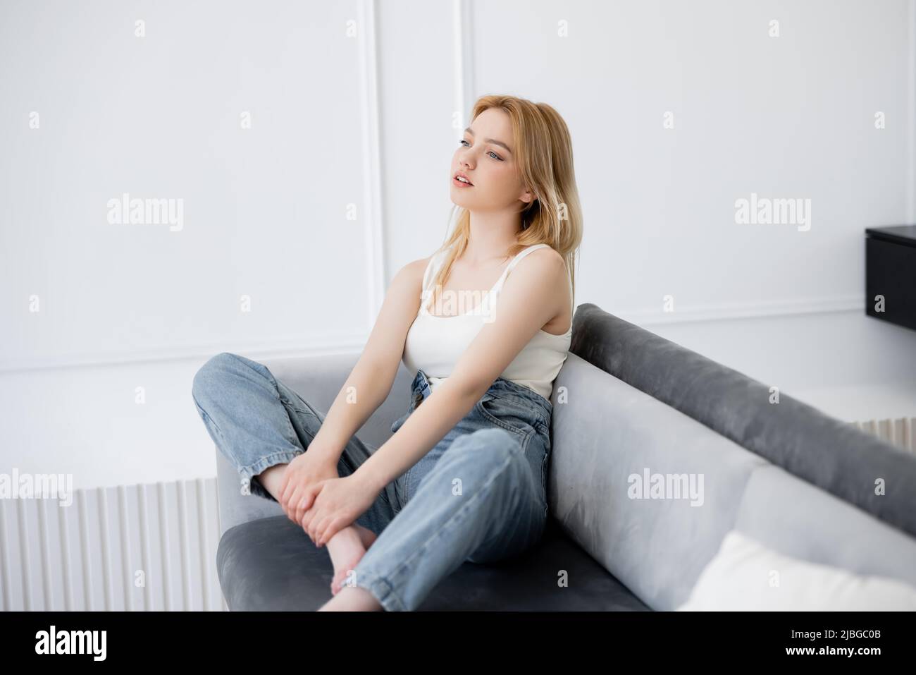 Young blonde woman looking away while sitting on couch Stock Photo