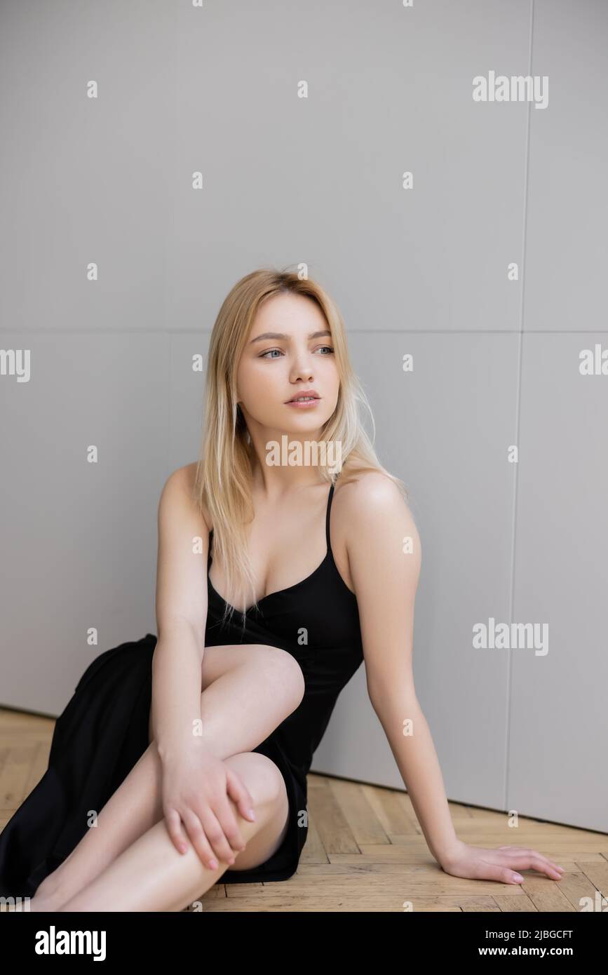 Elegant blonde woman in black dress sitting on floor at home Stock Photo