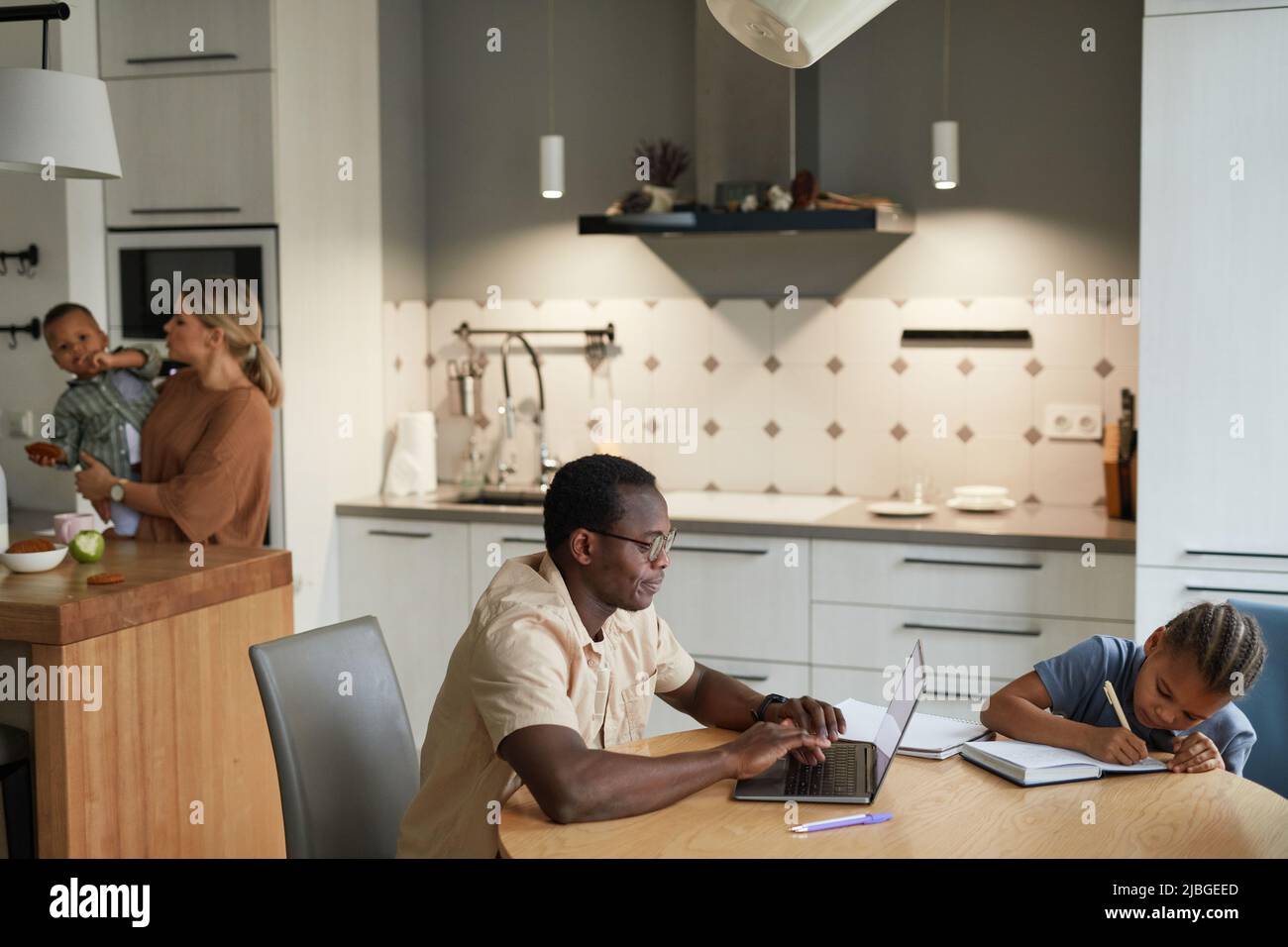 Lifestyle scene of multiethnic family with two kids and black father using laptop in foreground, copy space Stock Photo