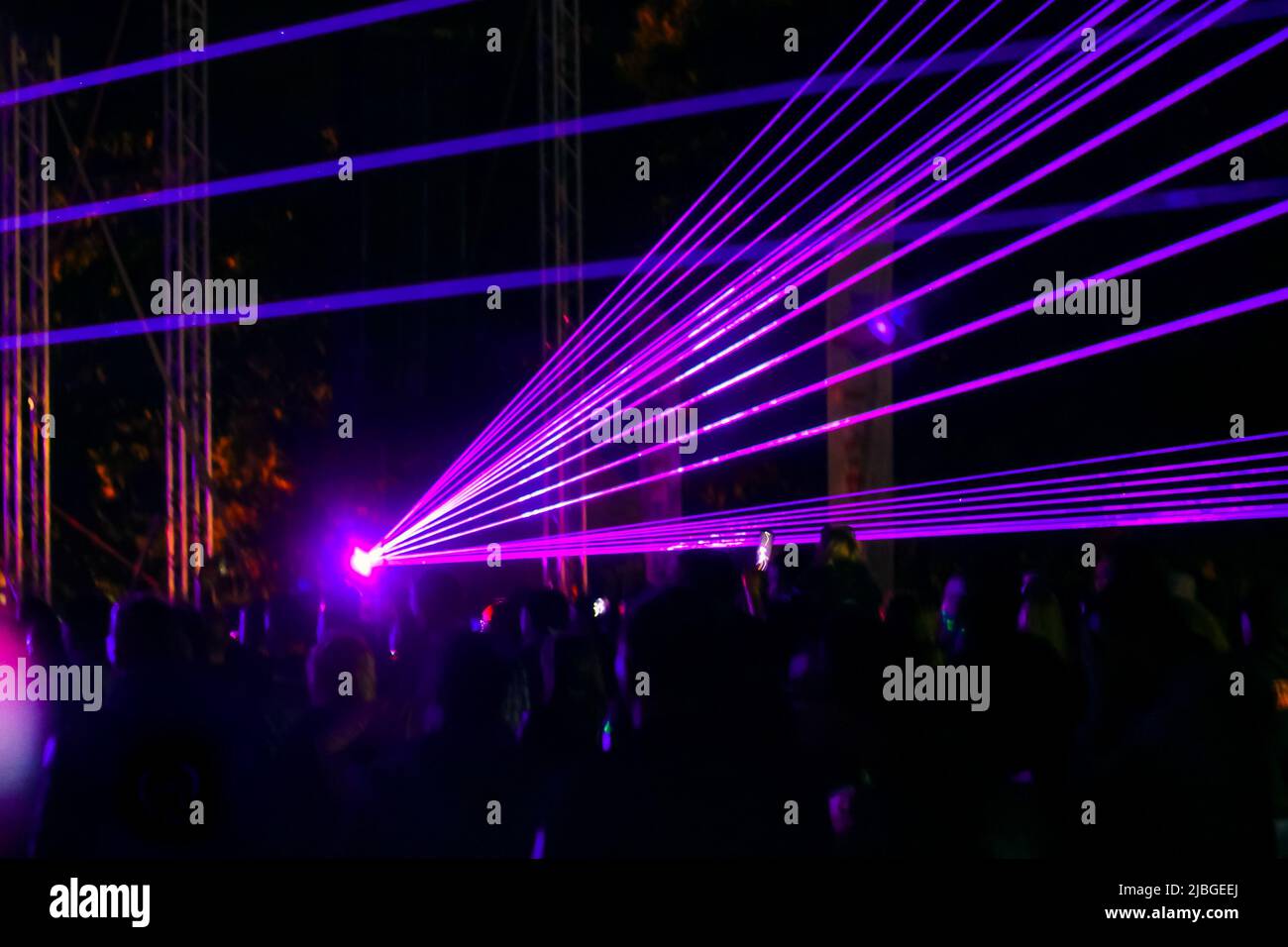 Purple laser neon beams. Crowd of people watching laser show at street festival. Many people enjoy the concert. Stock Photo