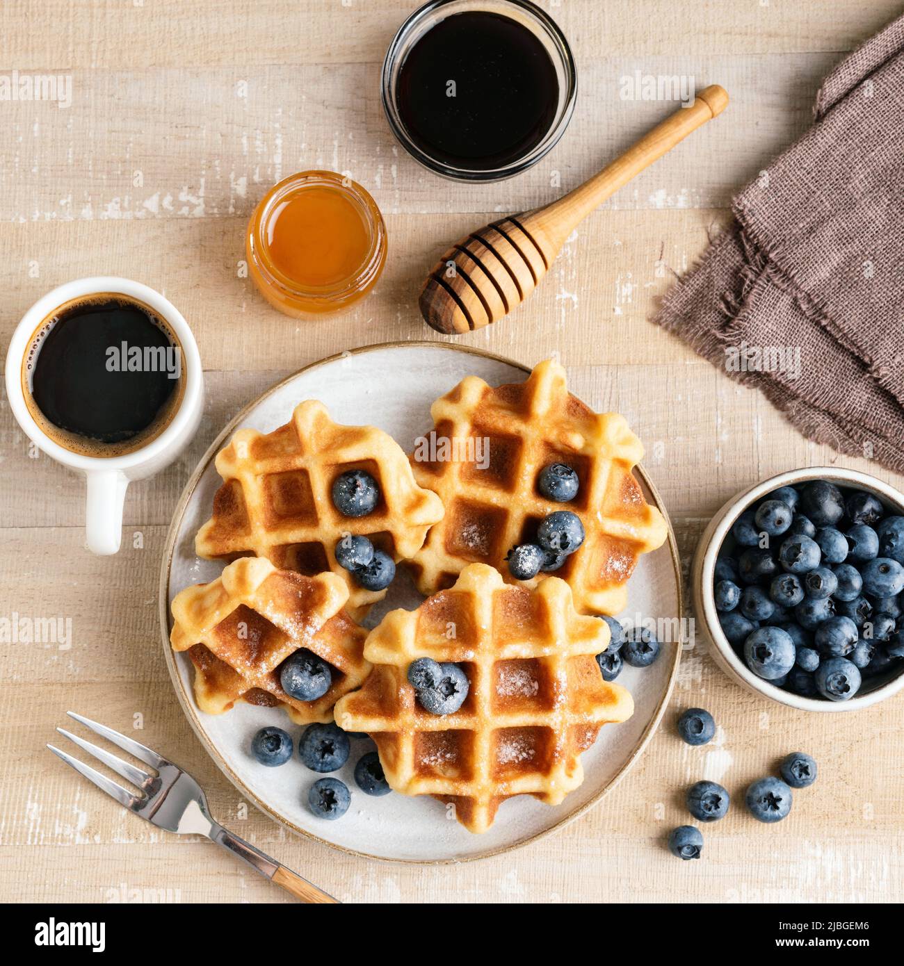 Sweet belgian waffles with blueberries, honey and cup of black coffee on a wooden table, top view. Square crop Stock Photo