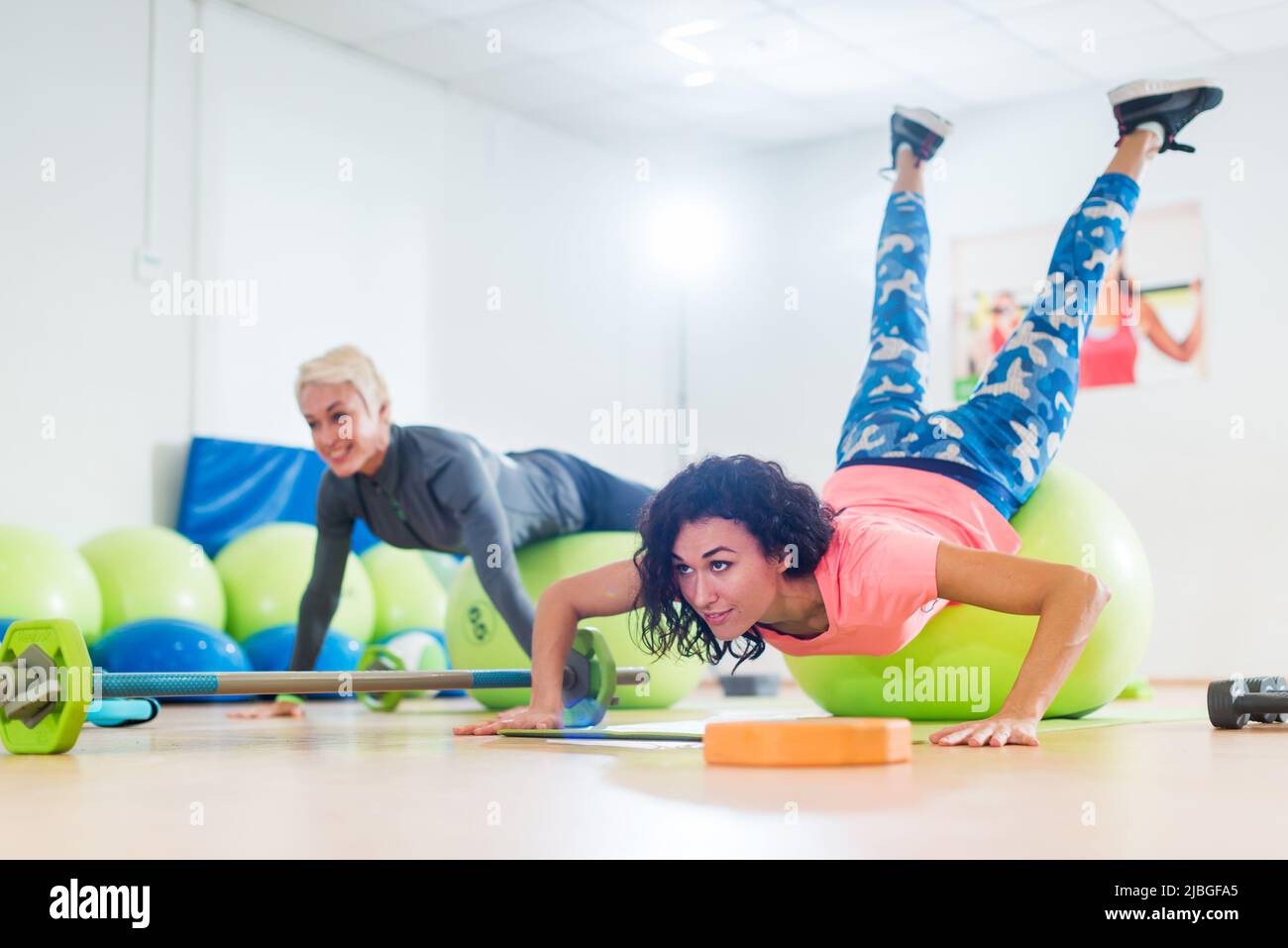 Two women exercising with stability balls doing push-ups in a gym class. Stock Photo