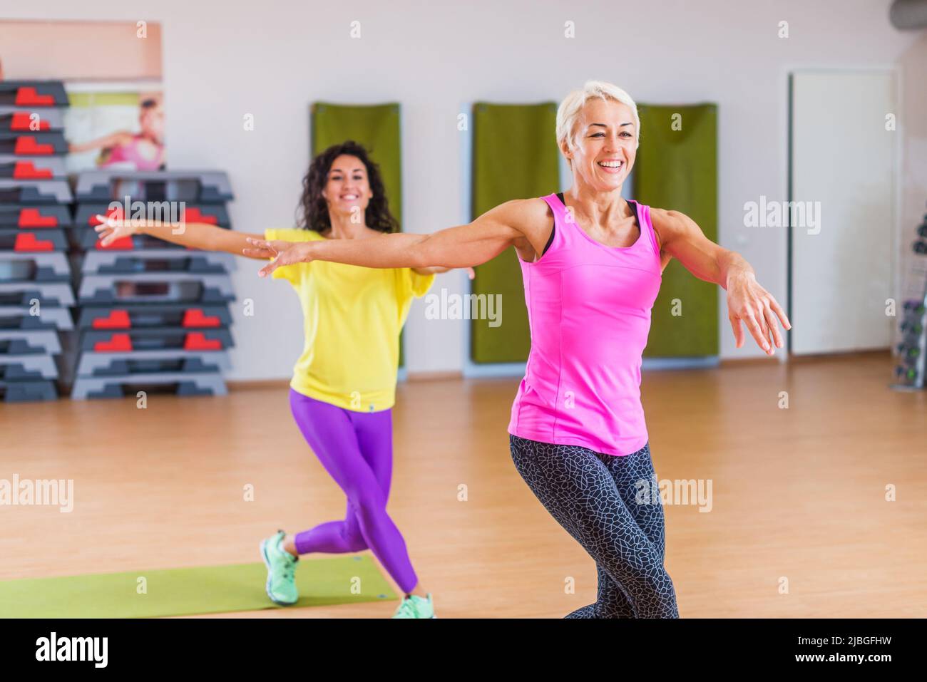Two smiling athletic women doing aerobic dancing exercises holding