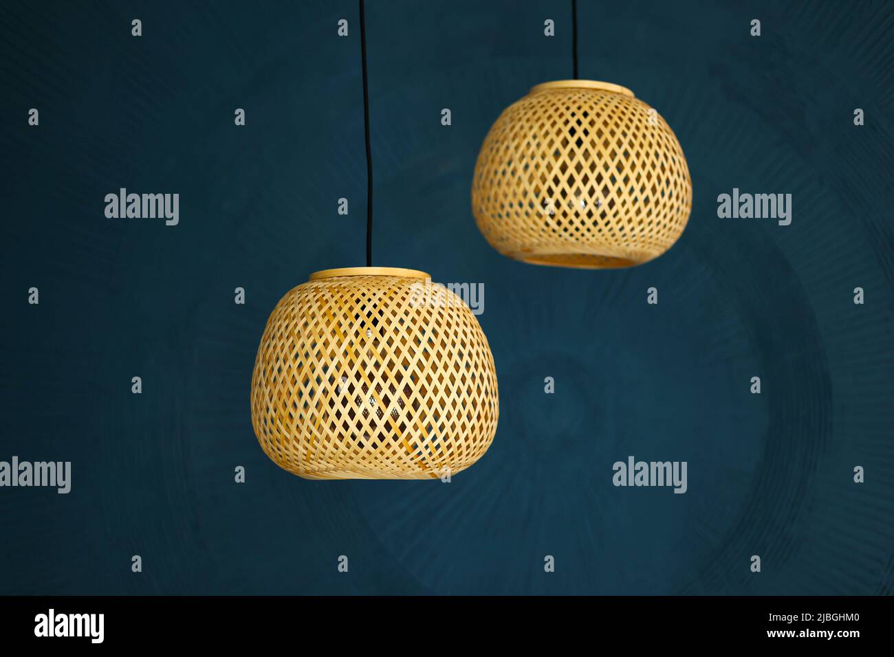 two rattan chandeliers on blue wall background. Straw lampshade in modern living room. Eco-friendly interior design using natural materials. Scandinav Stock Photo