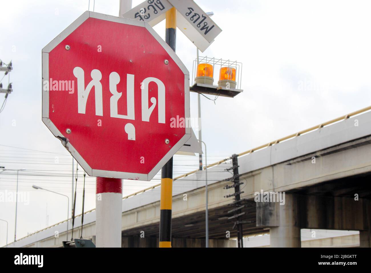 Warn sign in Thai at gated railroad crossing, Thailand. Translation : Stop / Beware train Stock Photo