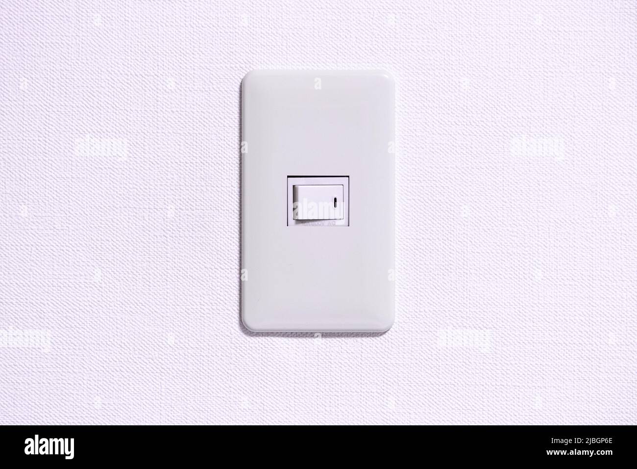 Simple light switch in room which is installed on the white coloured wall. Stock Photo