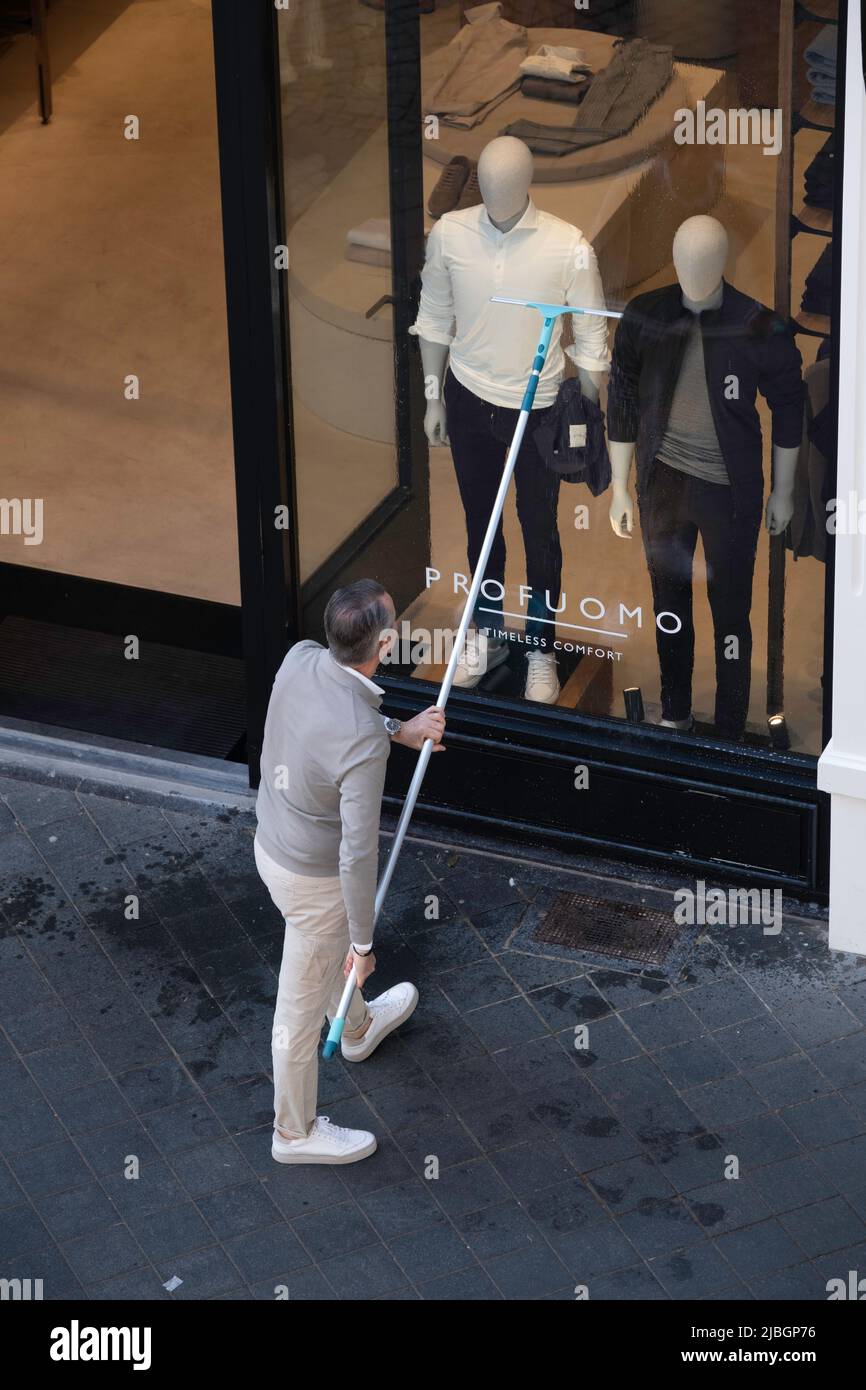 Shop owner cleaning his clothing store window with a long handle