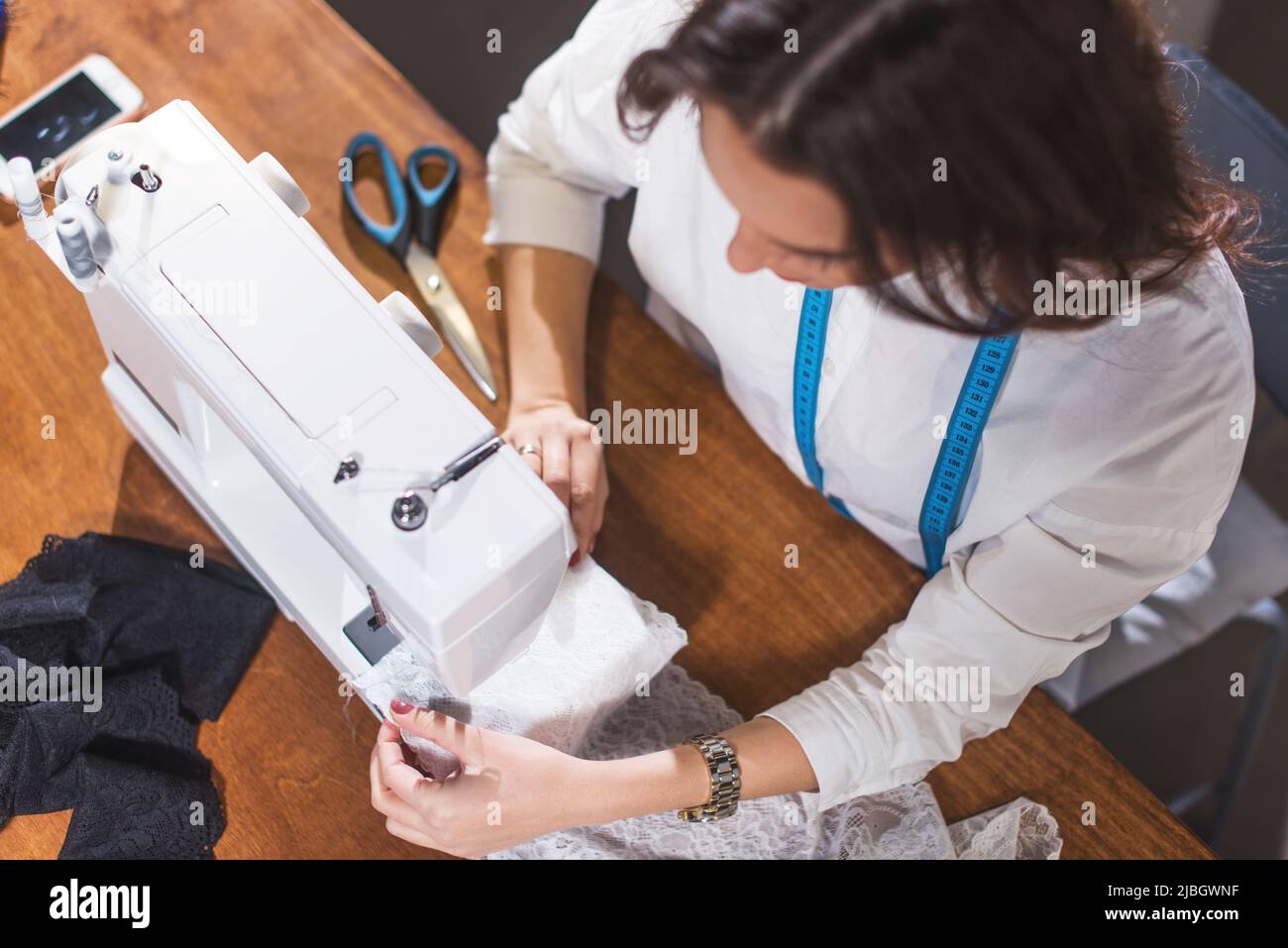 Top view of needlewoman stitching fabric on sewing machine at workplace in studio. Stock Photo