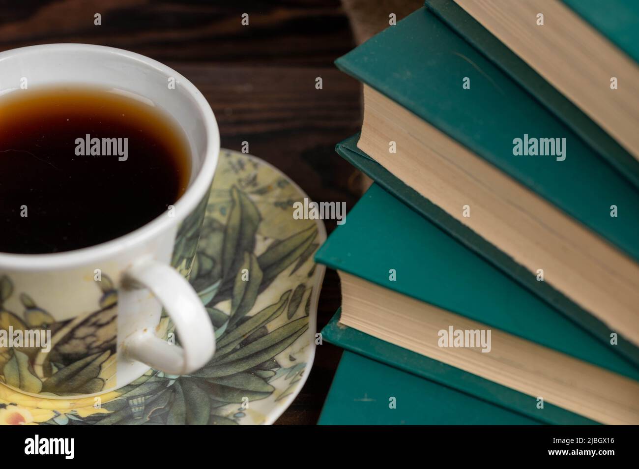 A cup of strong tea on a saucer and a stack of books on the table. Stock Photo