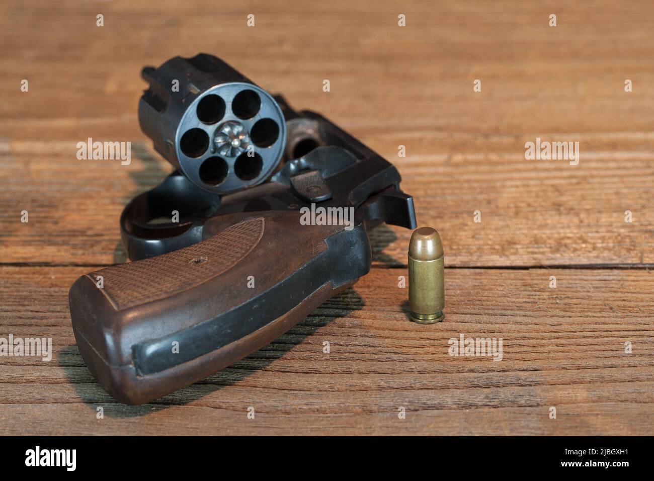 The last cartridge. A cartridge stands on a wooden table next to an open revolver. Stock Photo