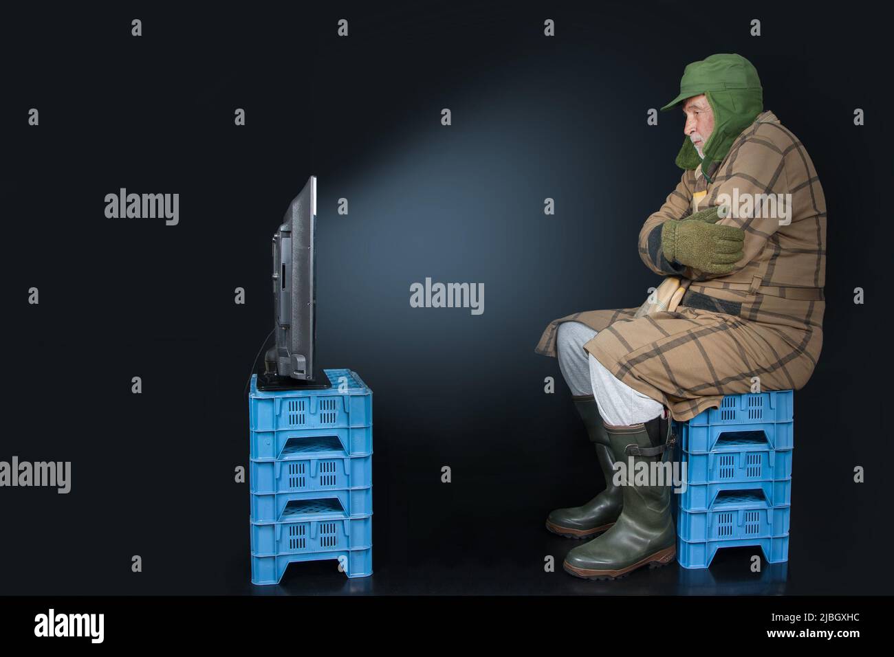 Freeze for Peace. TV evening autumn 2022 in Germany? A man, dressed warmly, is sitting on plastic boxes in front of the television. Stock Photo